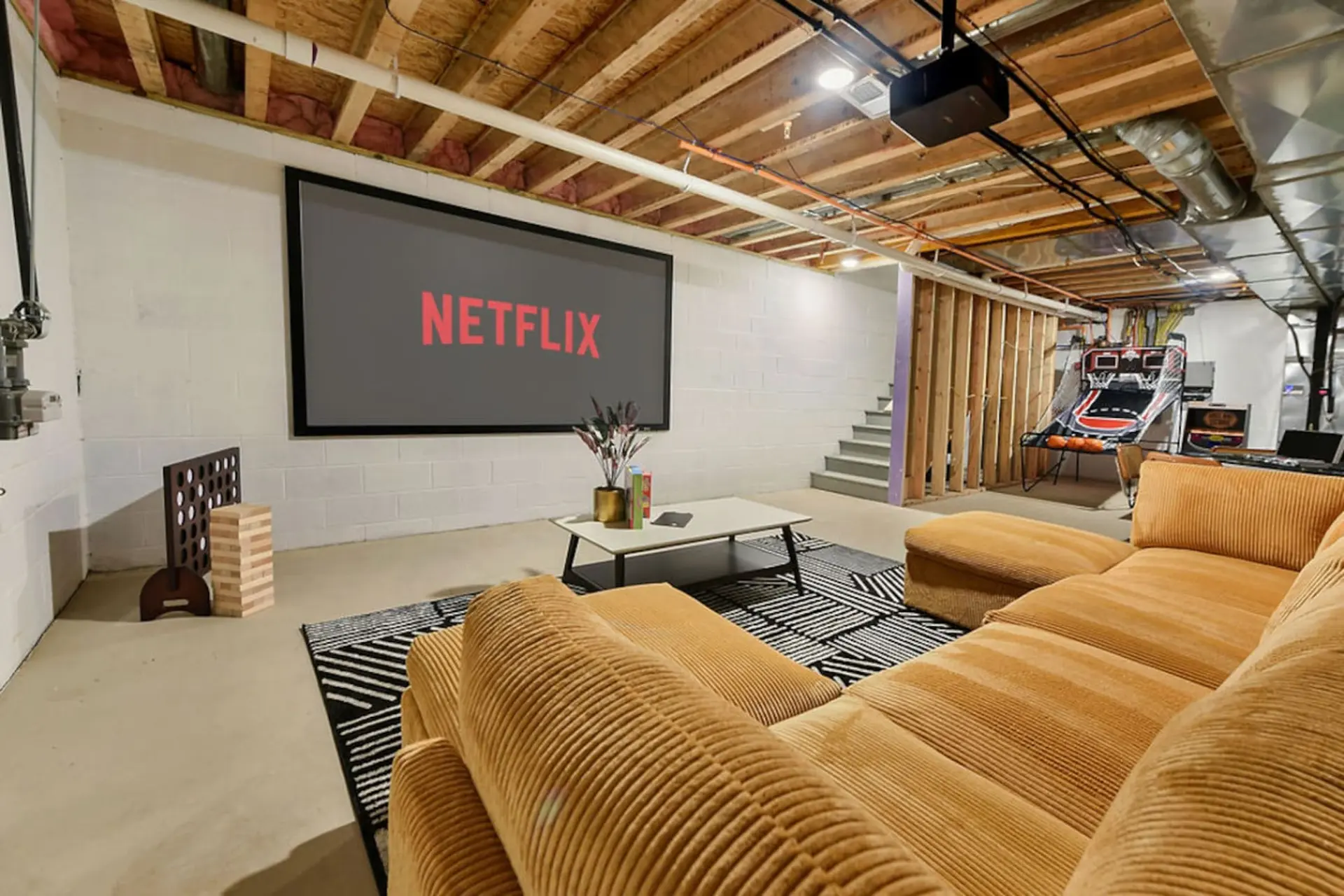 A basement entertainment room with a large screen displaying Netflix and a comfortable sectional sof