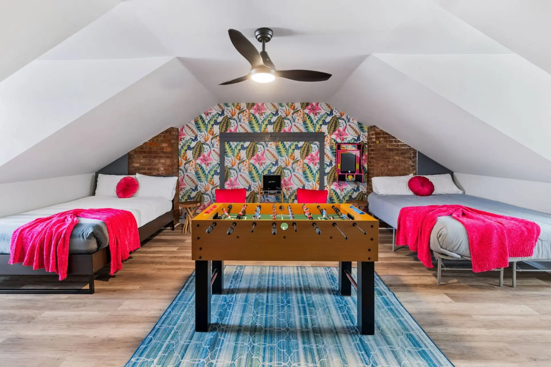 Attic bedroom with two beds, foosball table, and playful tropical wallpaper.