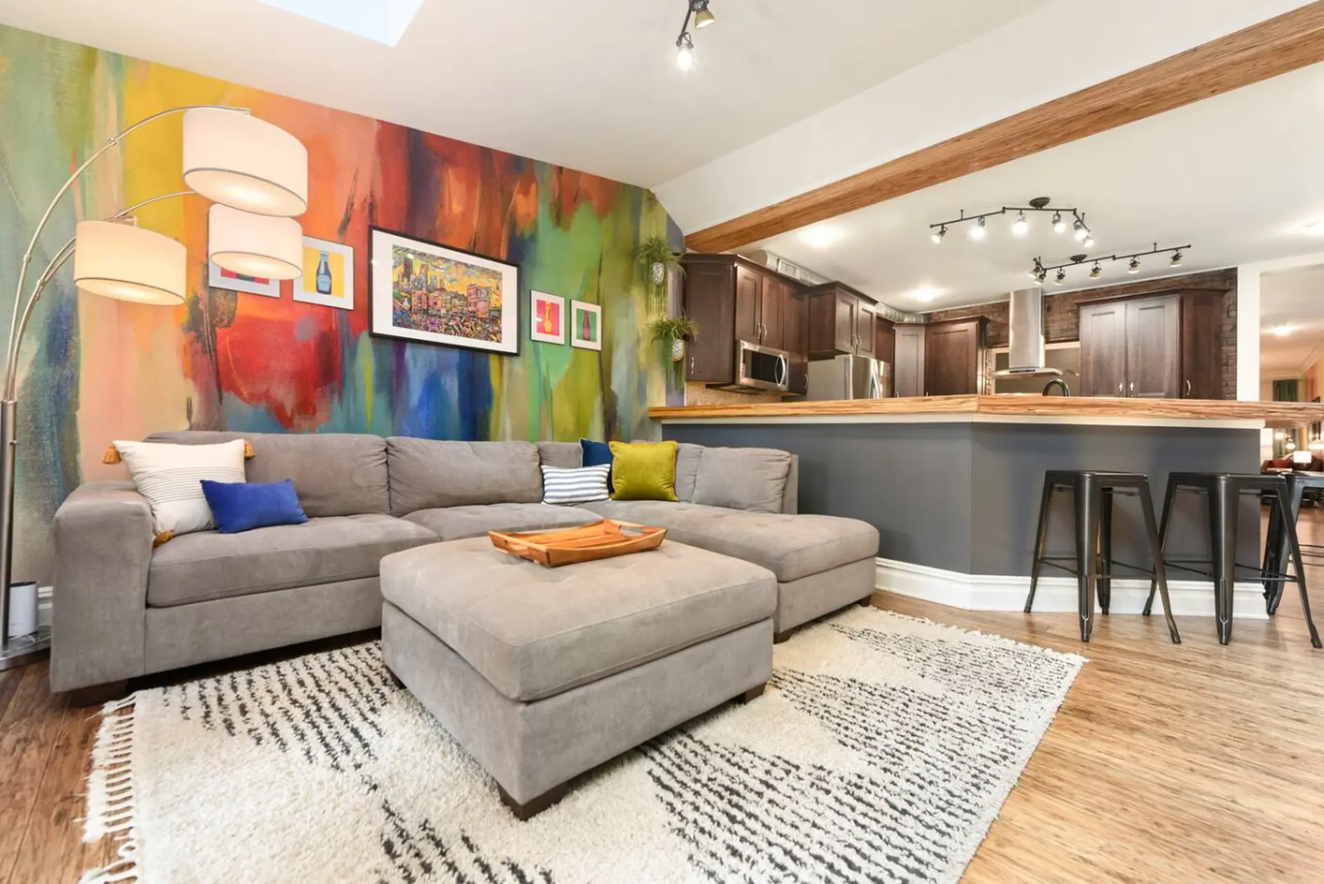 A gray sectional couch faces a vibrant, abstract mural and a modern kitchen.