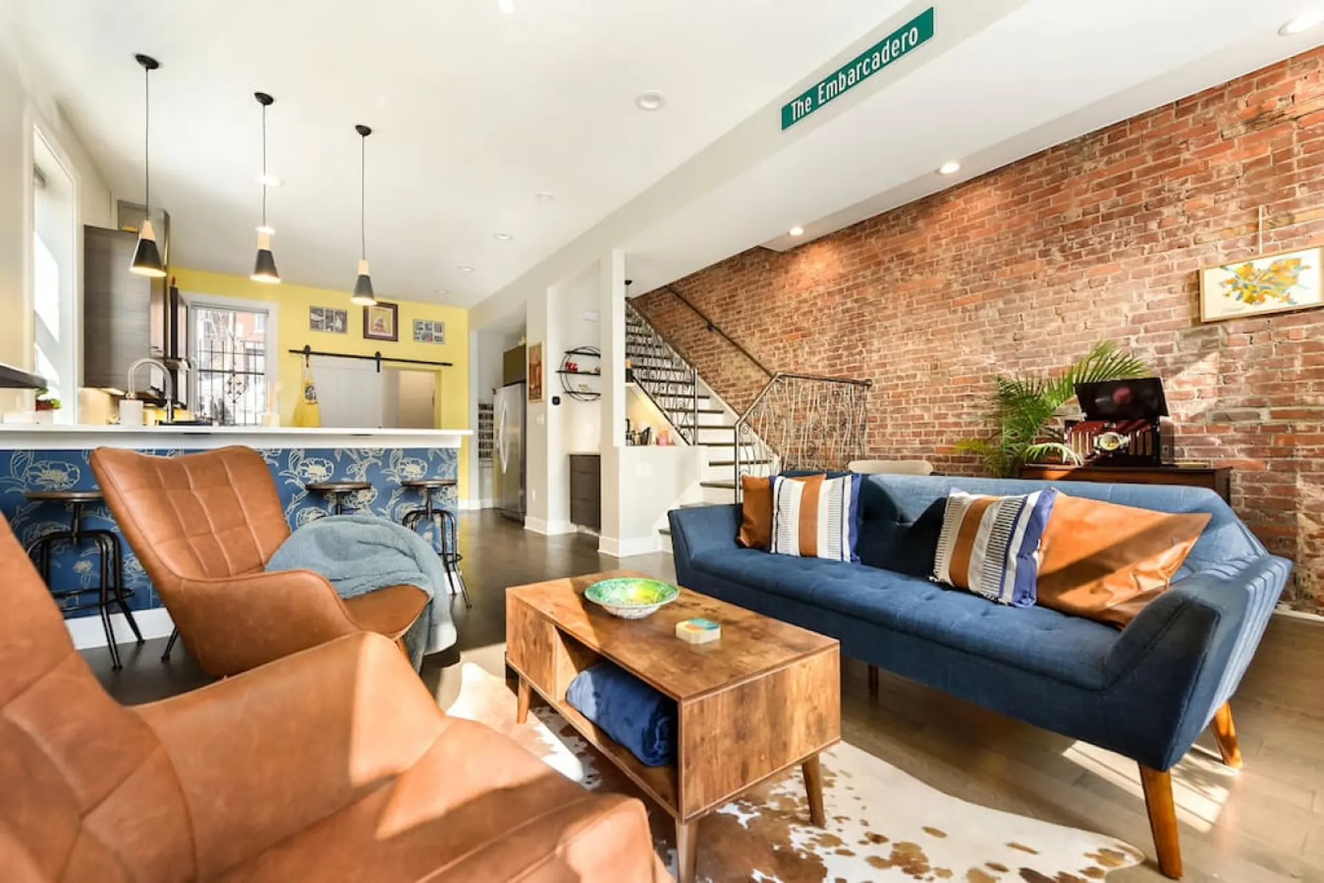 A living room with a blue sofa, brick wall, and leather chairs.