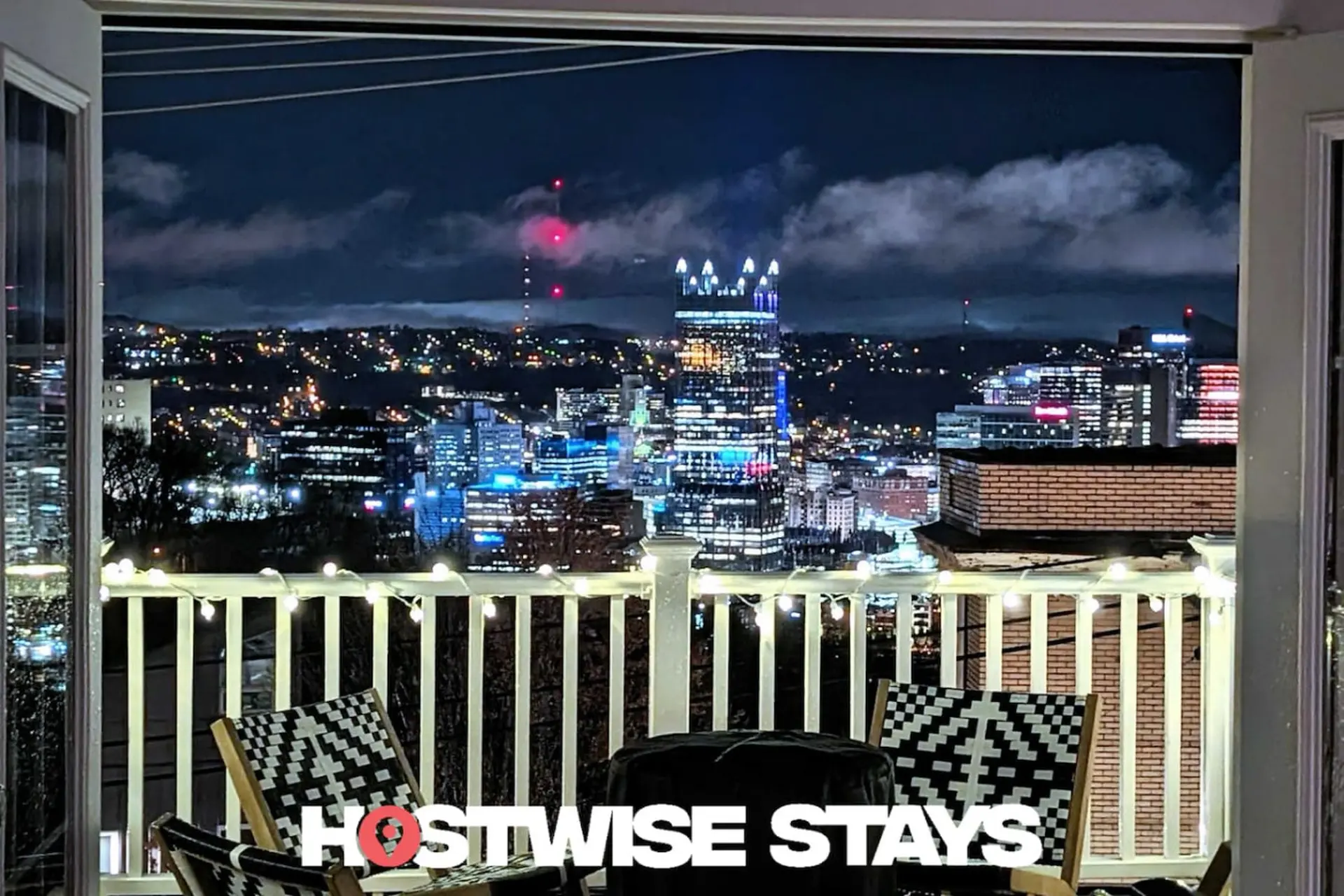 A balcony overlooks a city skyline at night, with lights from buildings and a radio tower.