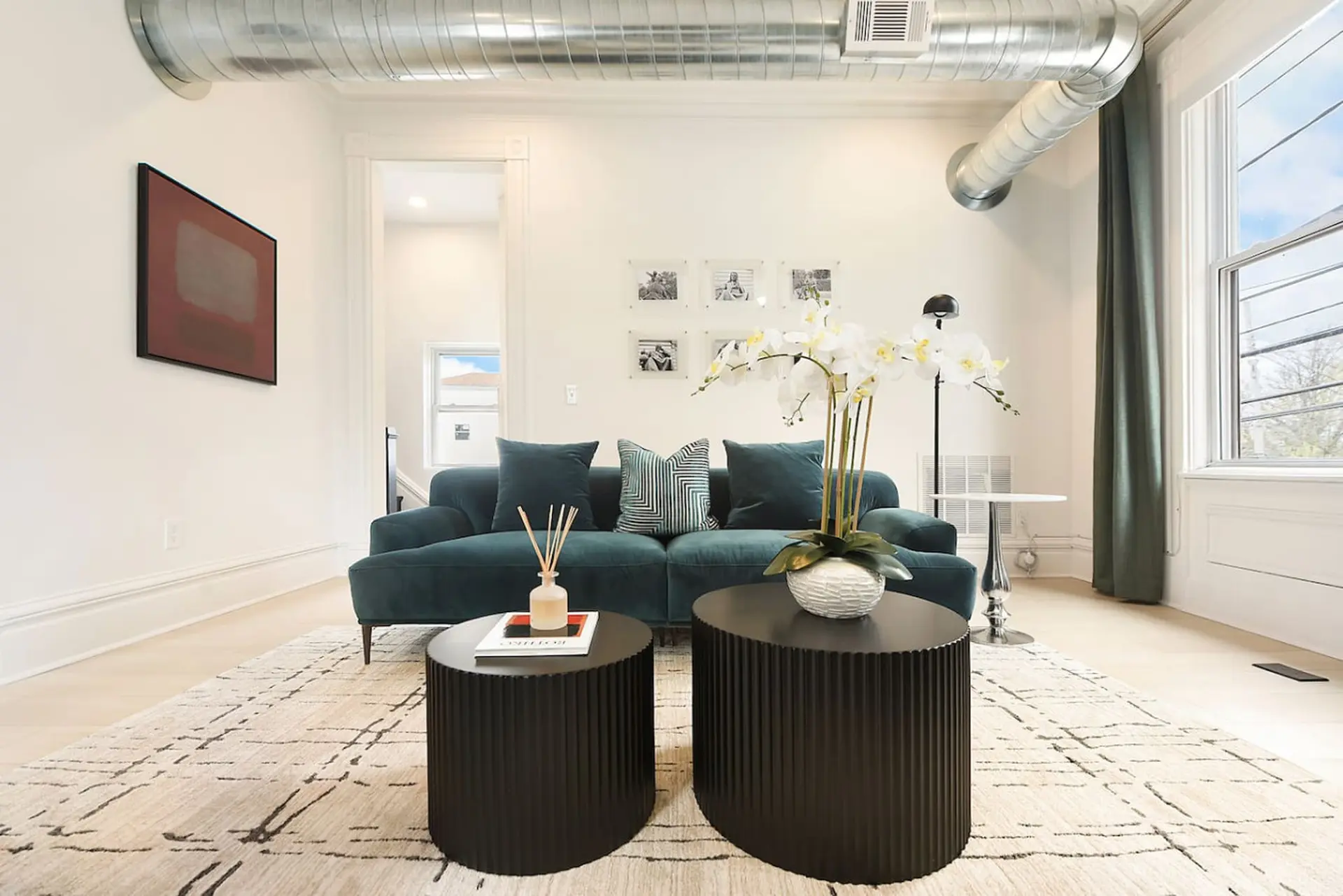 A teal sofa with throw pillows sits on a beige and black rug.