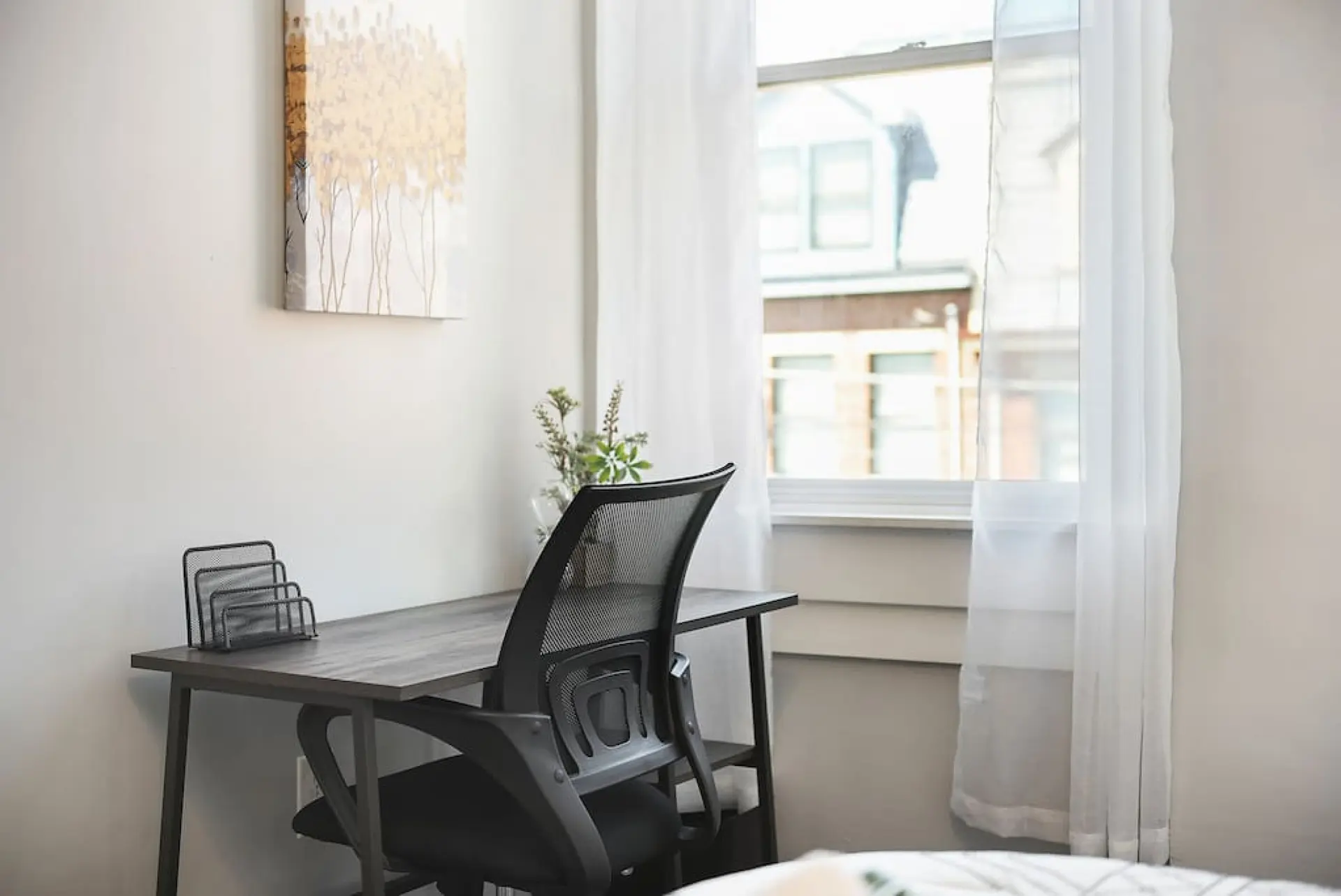 A black mesh office chair is at a desk with a metal organizer and a vase with plants.