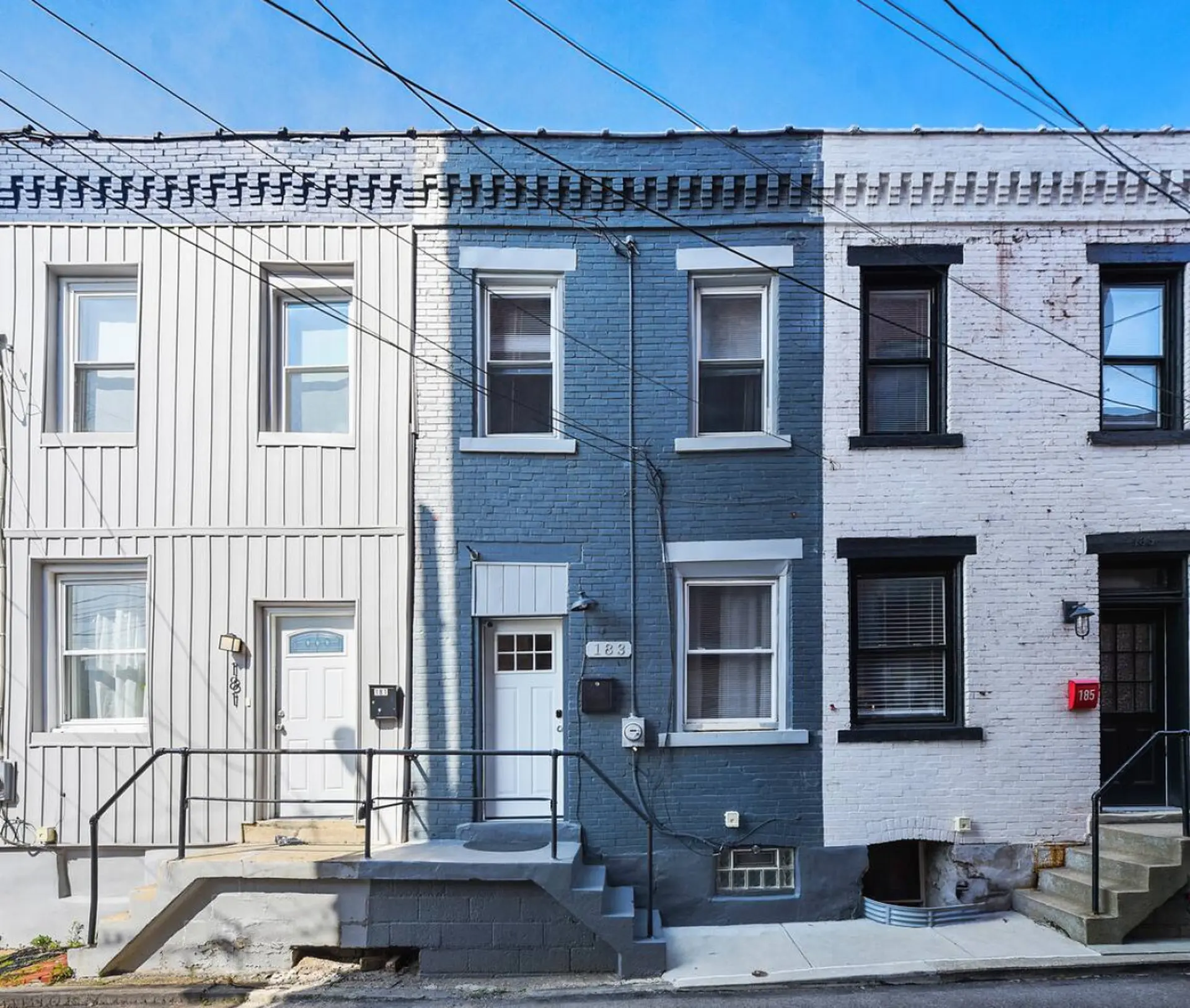 A row of attached townhouses painted white, blue, and grey, with windows and doors.