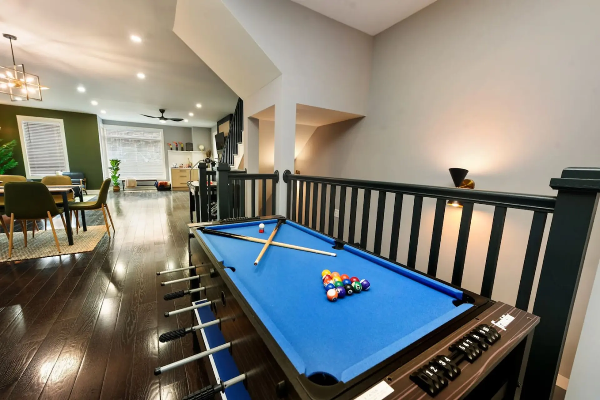 A blue pool table with colorful balls and cue sticks sits on dark hardwood floors.