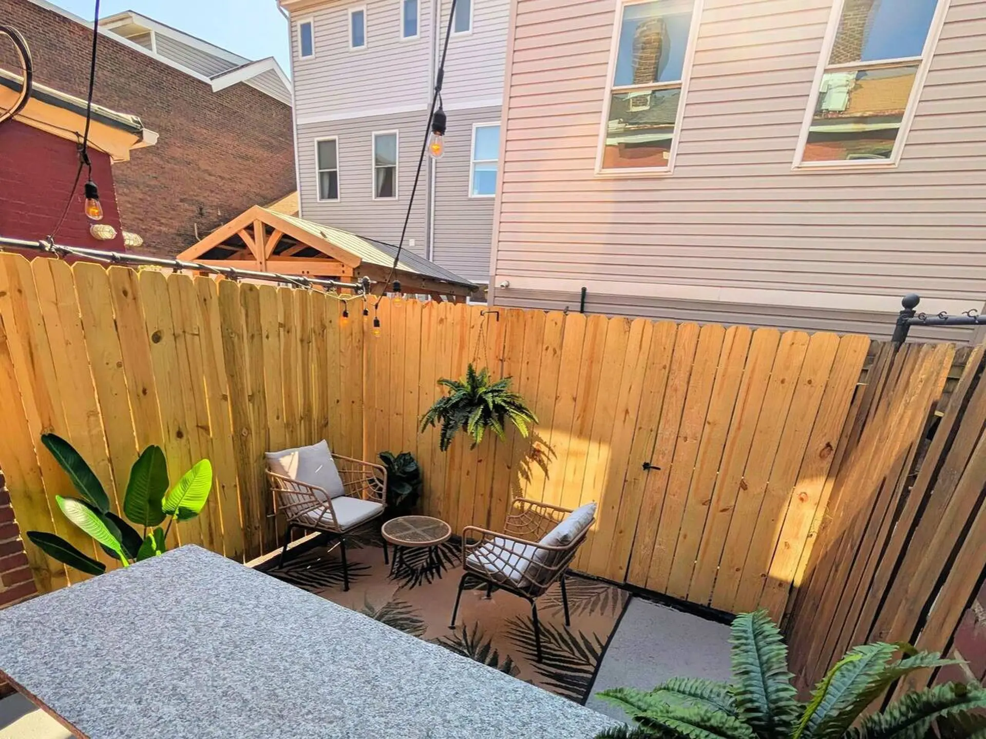 A fenced patio with chairs, a table, and plants.