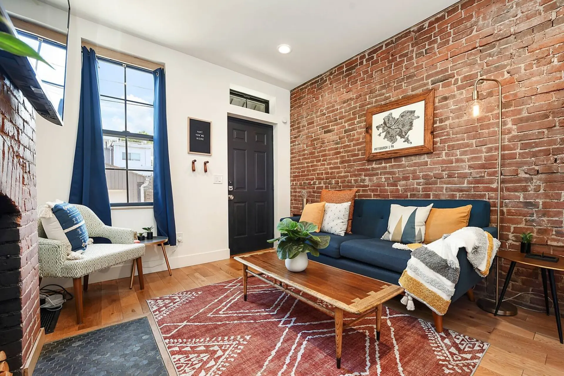 A cozy living room with a blue sofa, brick wall, and a patterned rug.