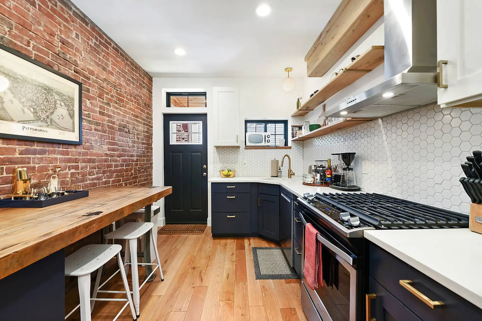 A compact kitchen features navy cabinets, white hex tiles, and a wooden island with stools.