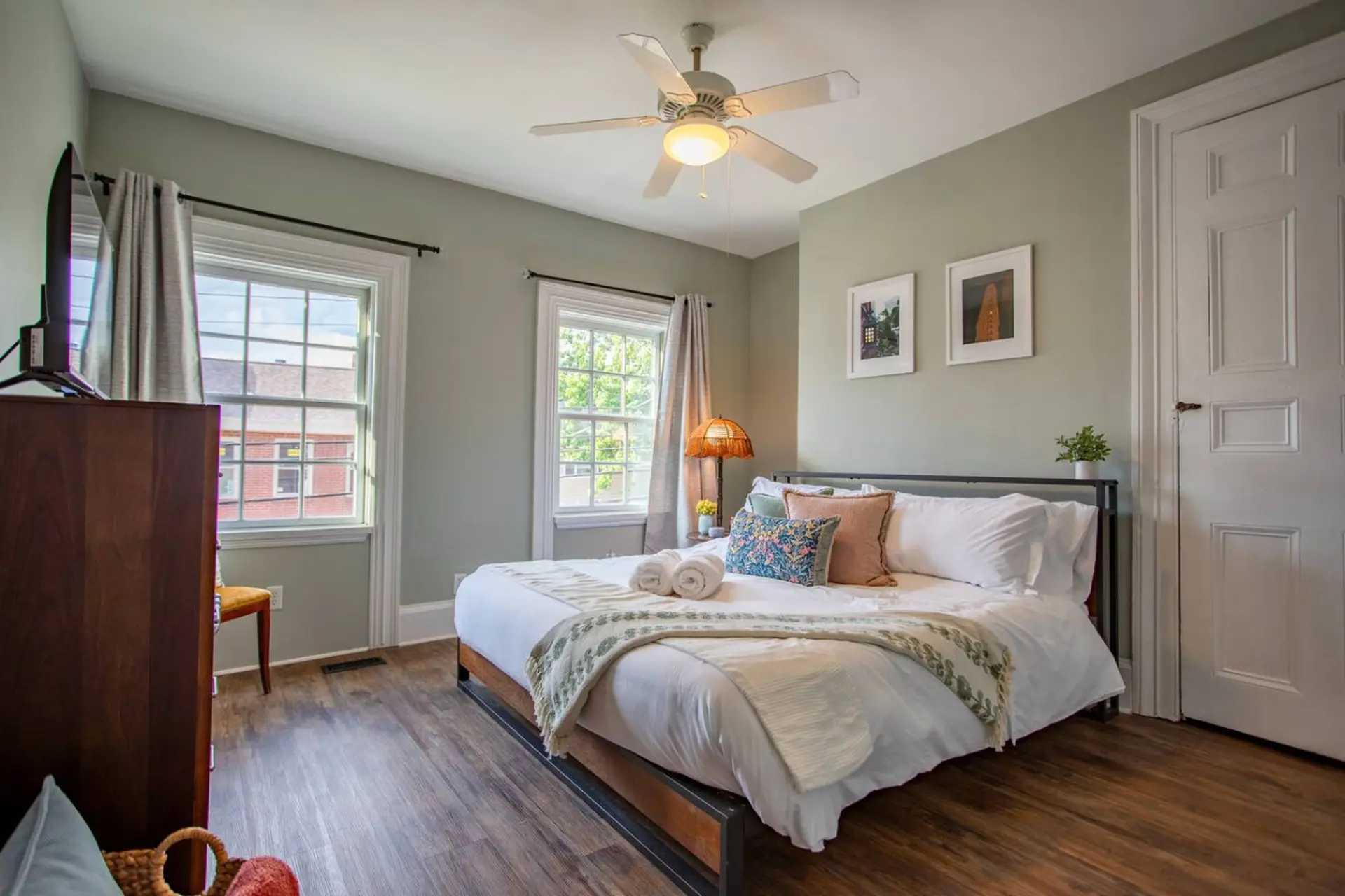 A bedroom with a queen-sized bed, tv, and two windows.