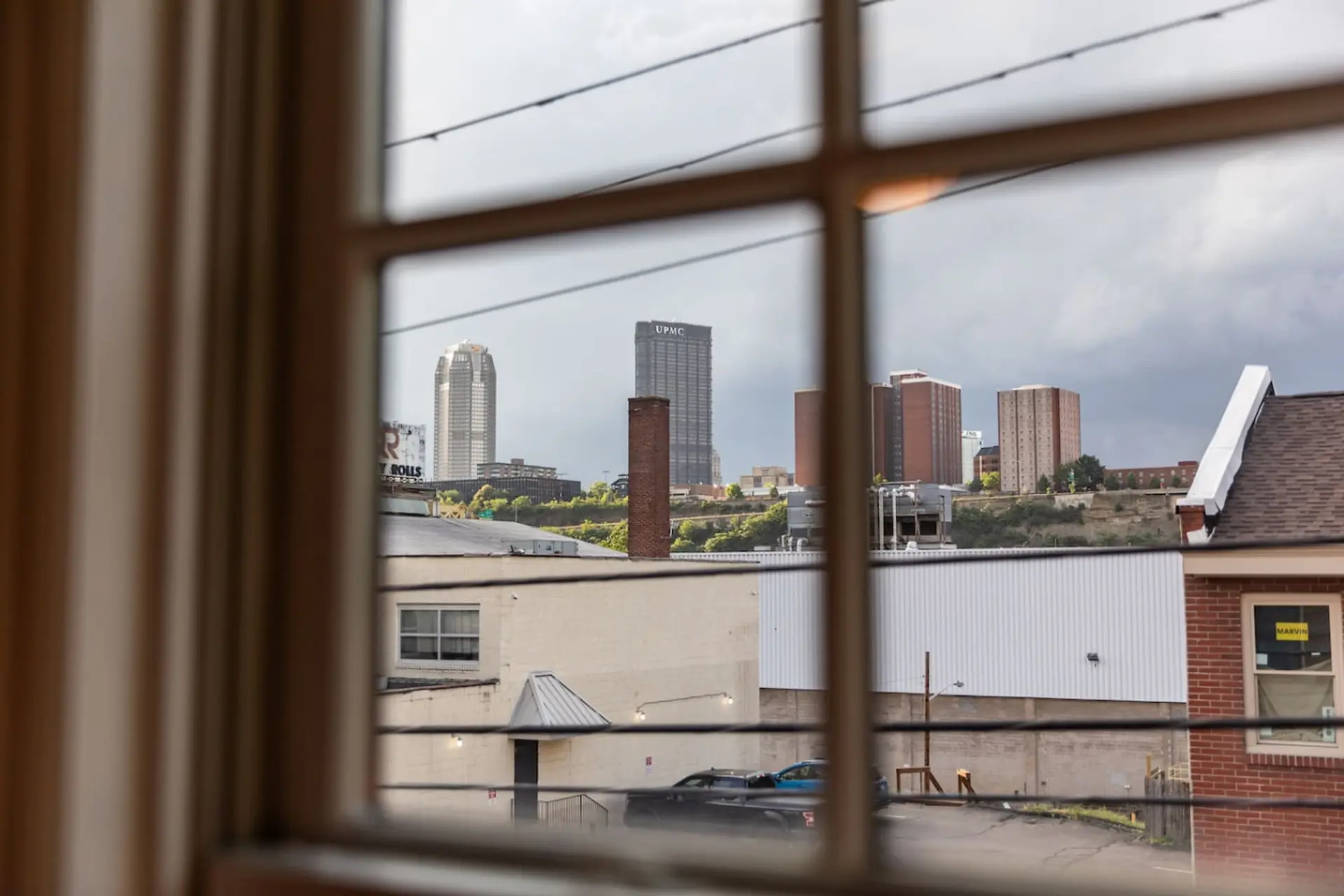 View of a cityscape through a window with horizontal bars, showing buildings and a cloudy sky.