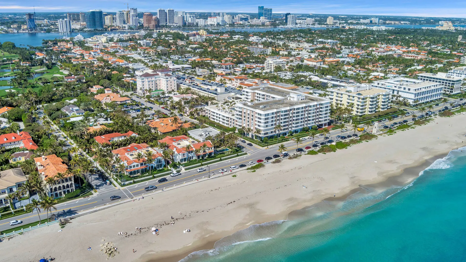 Aerial view of a coastal city with skyscrapers, golf courses, houses, and a beach.