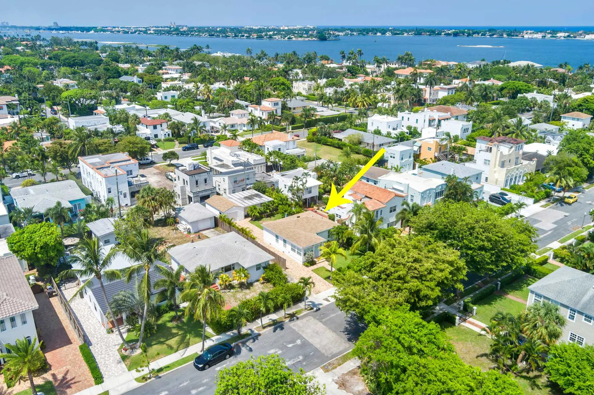 An aerial view of a neighborhood with homes, lush greenery, and a distant blue body of water.