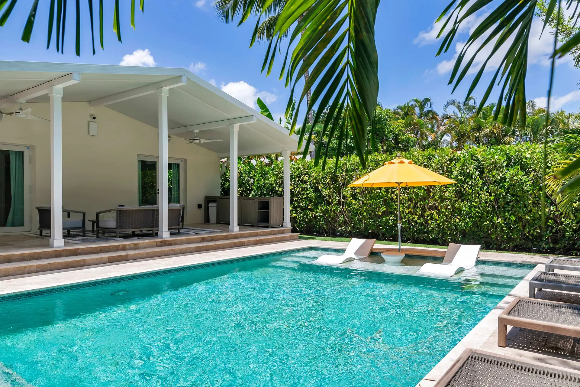 A sparkling turquoise pool with white lounge chairs and a yellow umbrella.