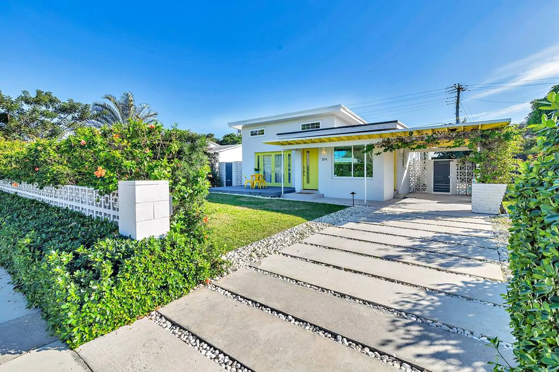 A white house with yellow accents and a carport sits on a sunny day.