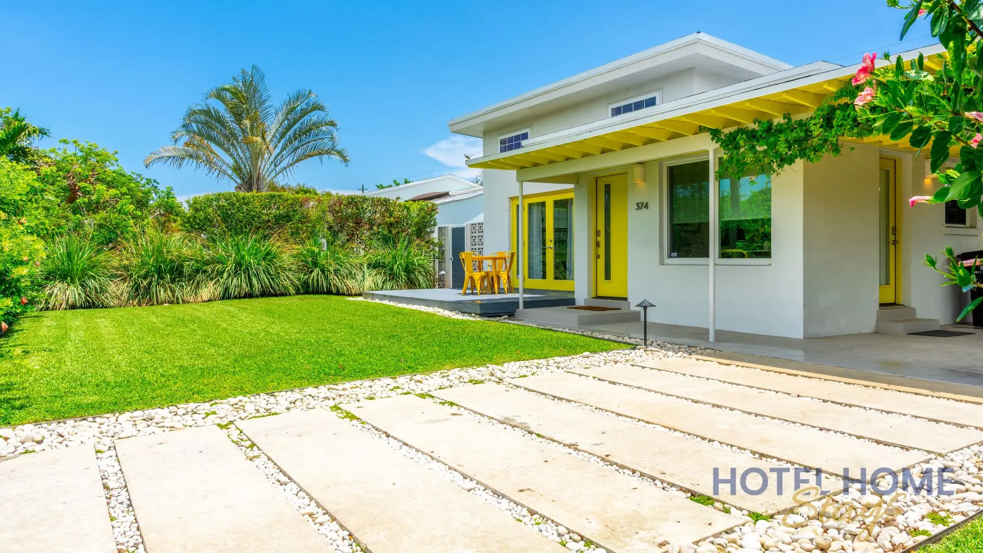 Modern white house with yellow accents and lush landscaping.