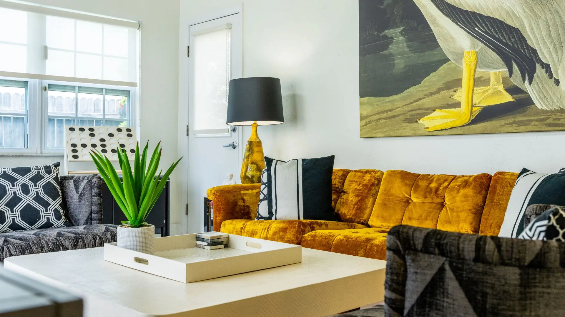 A bright living room with a mustard velvet sofa, modern art, and large windows.