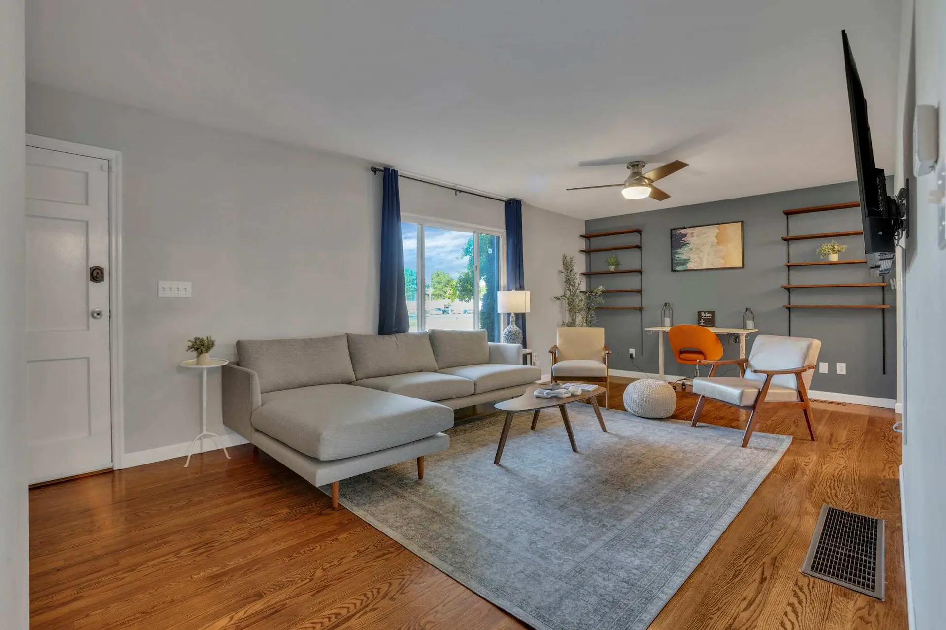 A modern living room with a grey sectional sofa, wooden floors, and a mounted TV.
