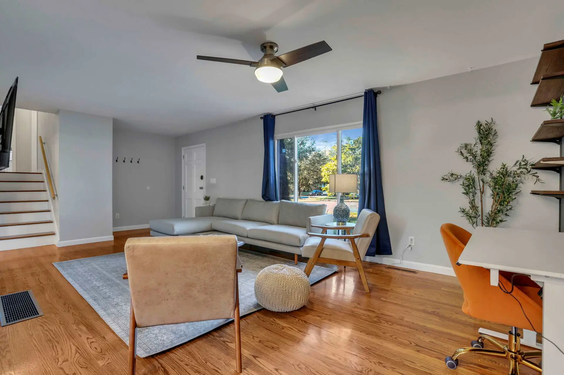 A living room with a sectional couch, an orange desk chair, and a ceiling fan.