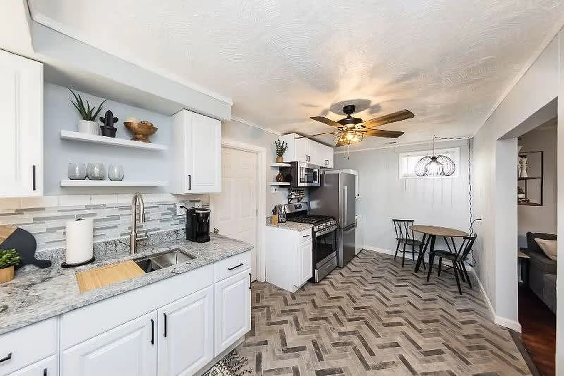 Modern white kitchen with granite countertops, stainless steel appliances, and a herringbone tile fl