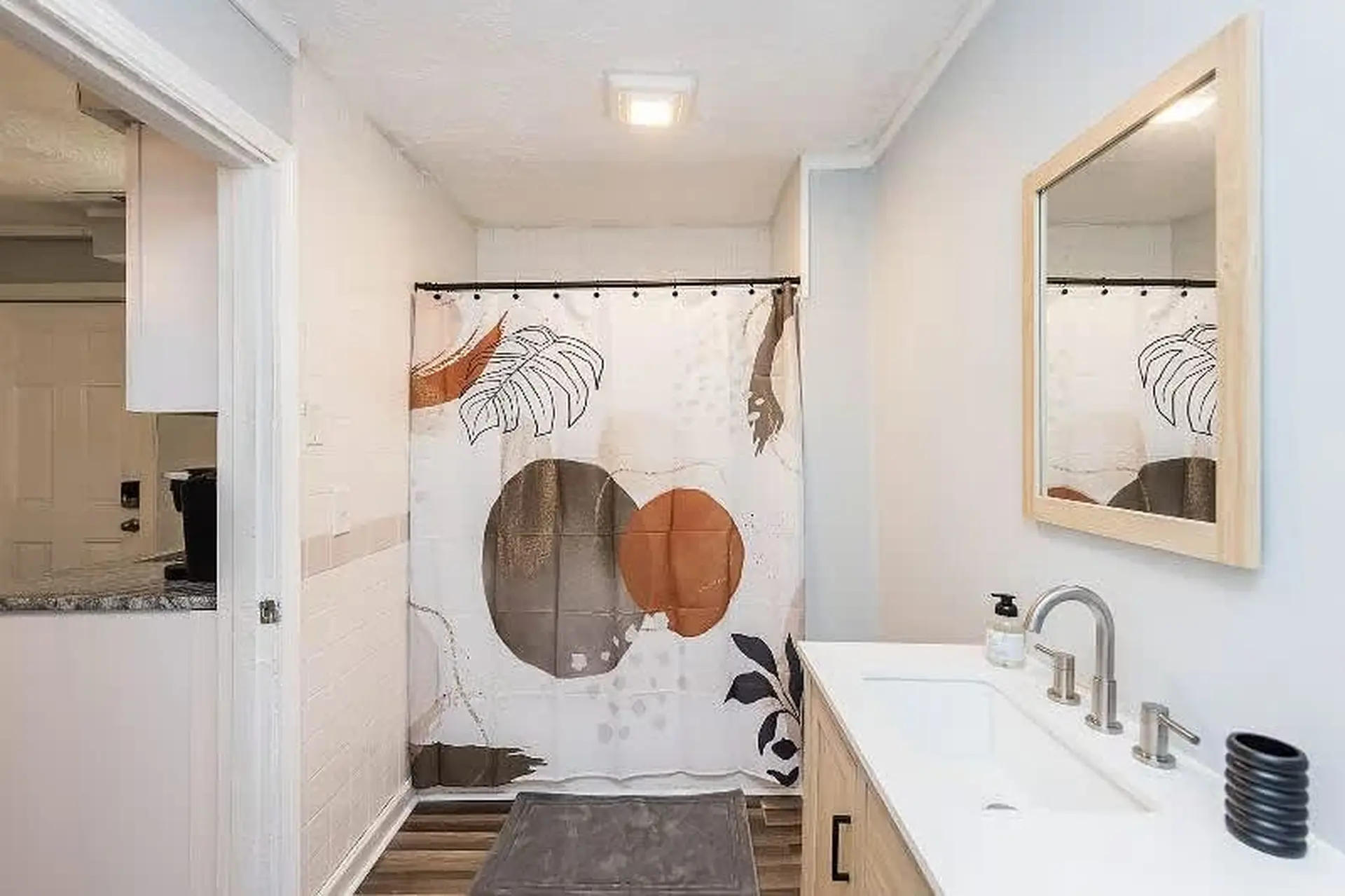A modern bathroom with a vanity, sink, mirror, and abstract shower curtain.