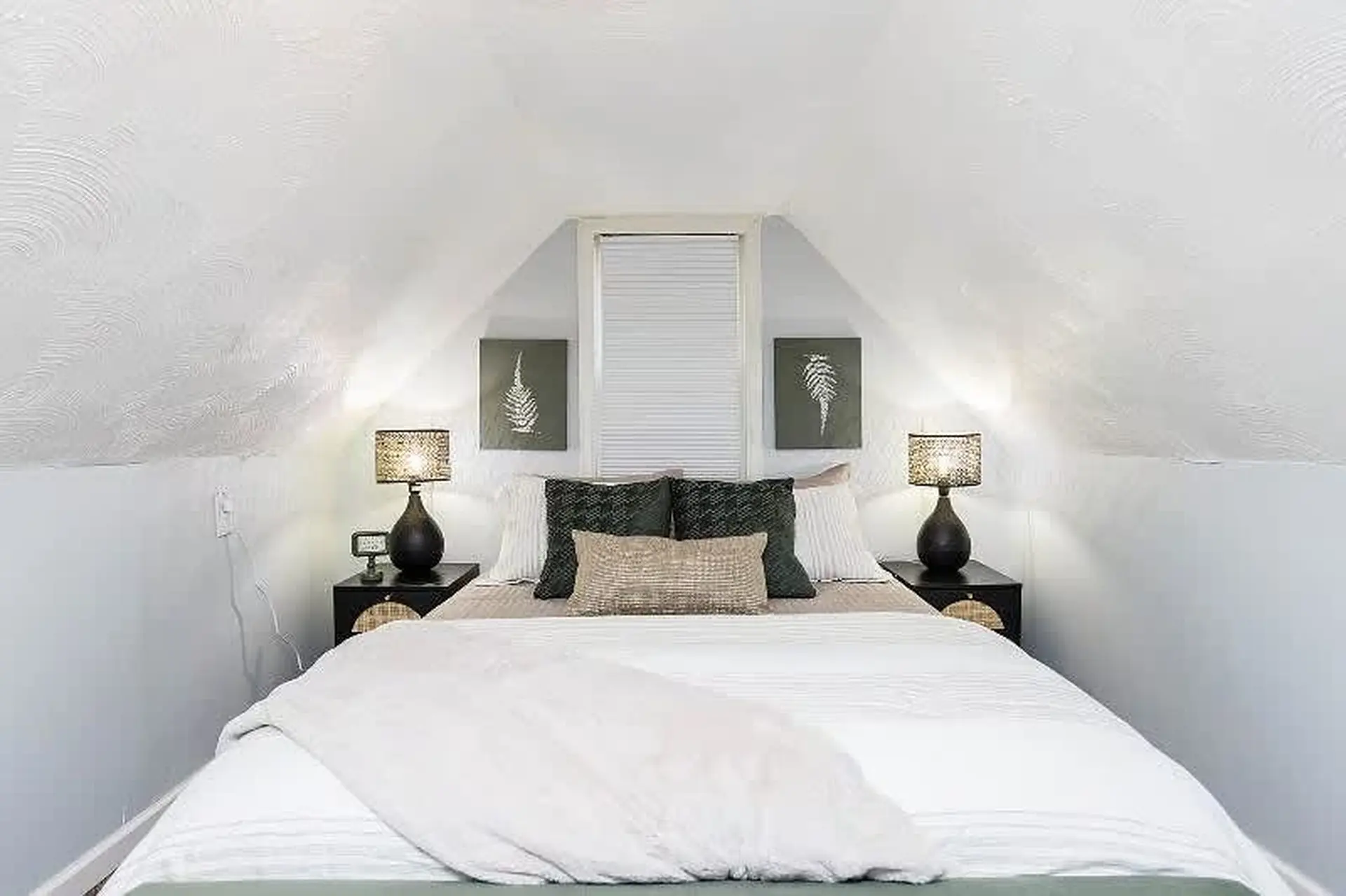 A cozy bedroom with a bed, two lamps, and two pieces of wall art.