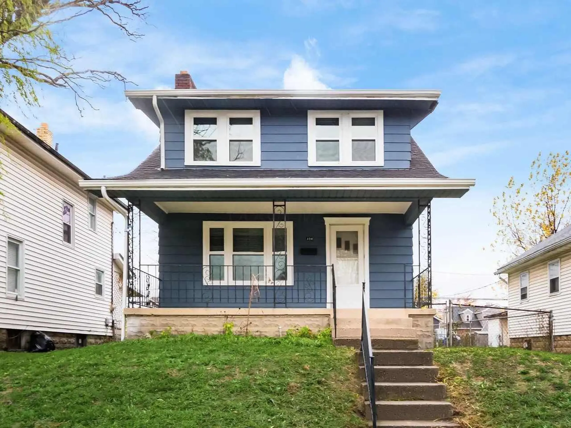 Blue two-story house with a porch and white trim, on a grassy lawn.