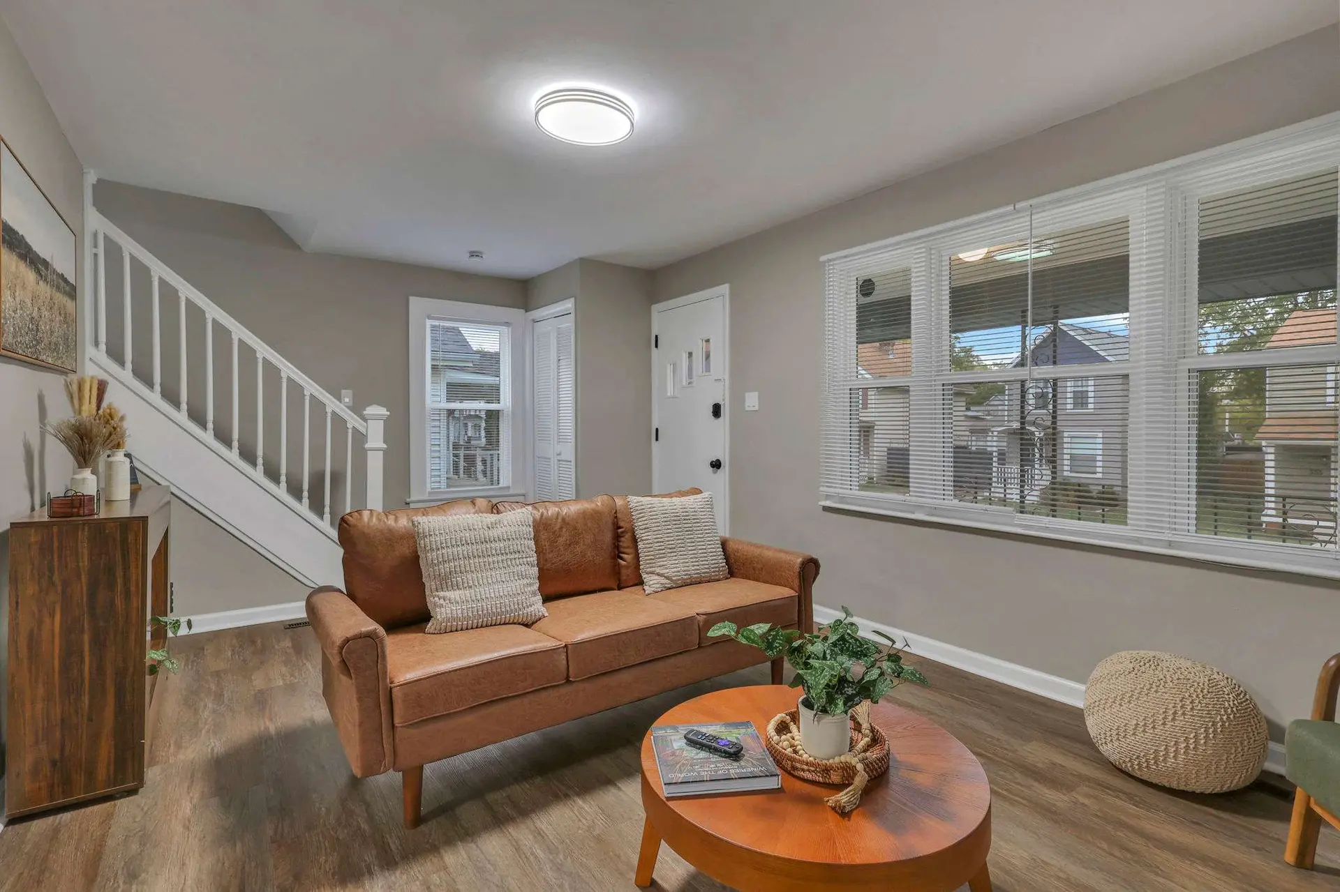 A cozy living room with a brown leather couch, a round coffee table, and stairs.