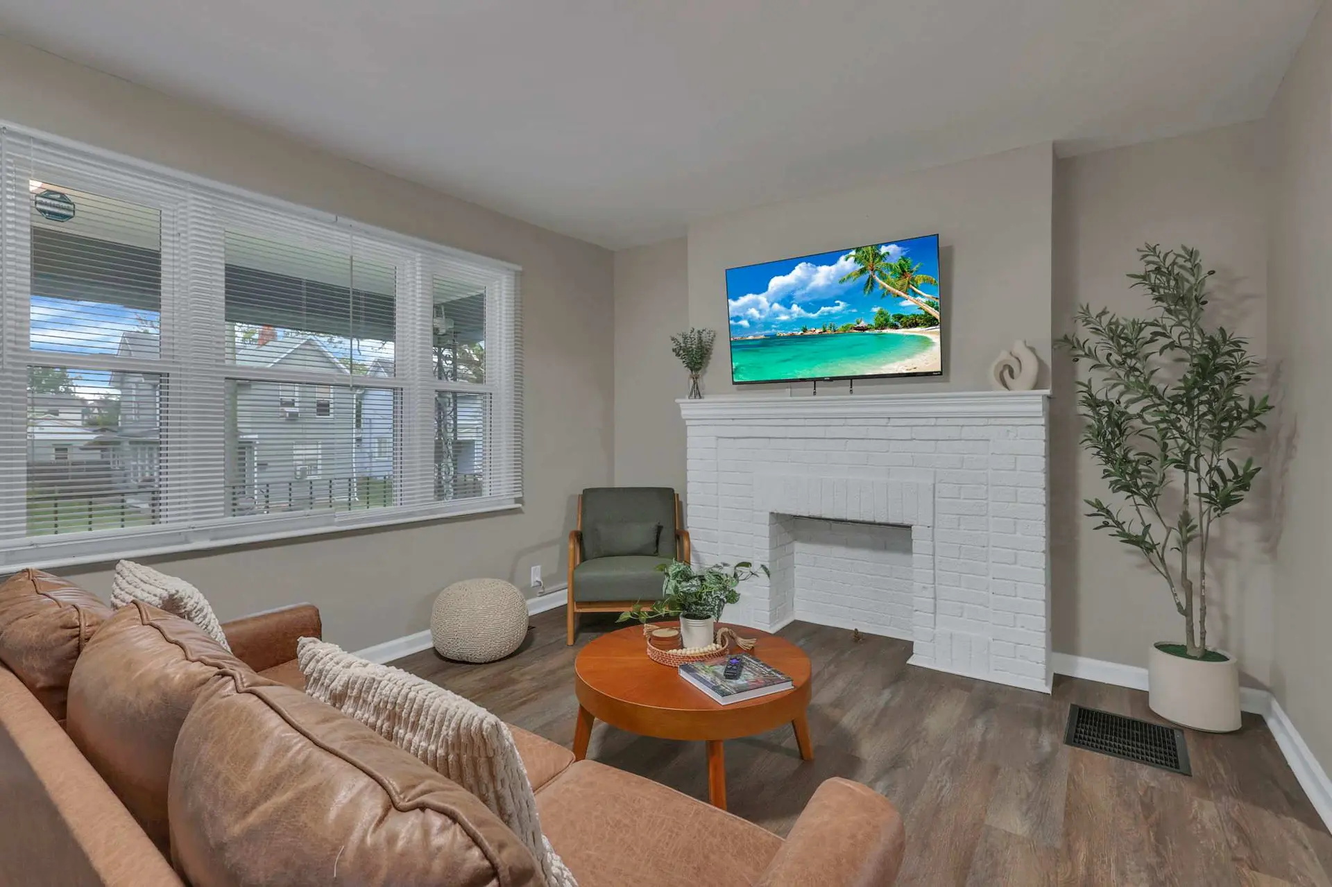 A living room with a brown leather sofa, a circular wooden coffee table, and a white brick fireplace
