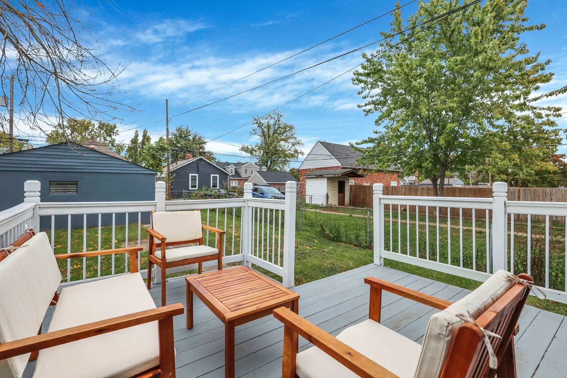 Outdoor deck with wooden furniture and a view of houses and a large tree.