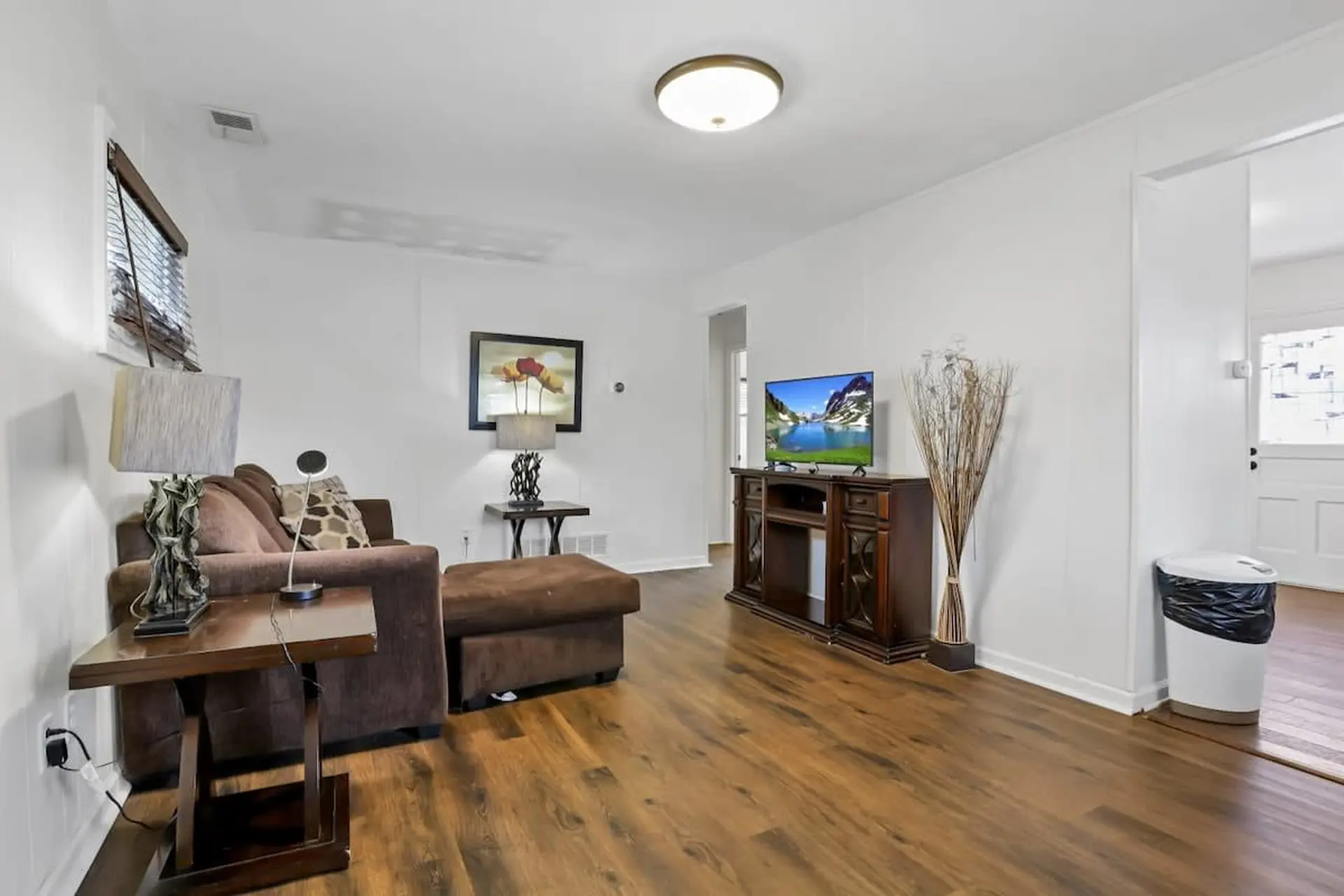 A living room with a brown sofa, a television on a dark wood stand, and a brown ottoman.