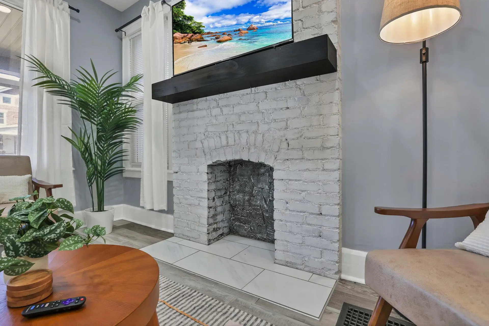 A modern living room with a white brick fireplace, TV, and natural light.