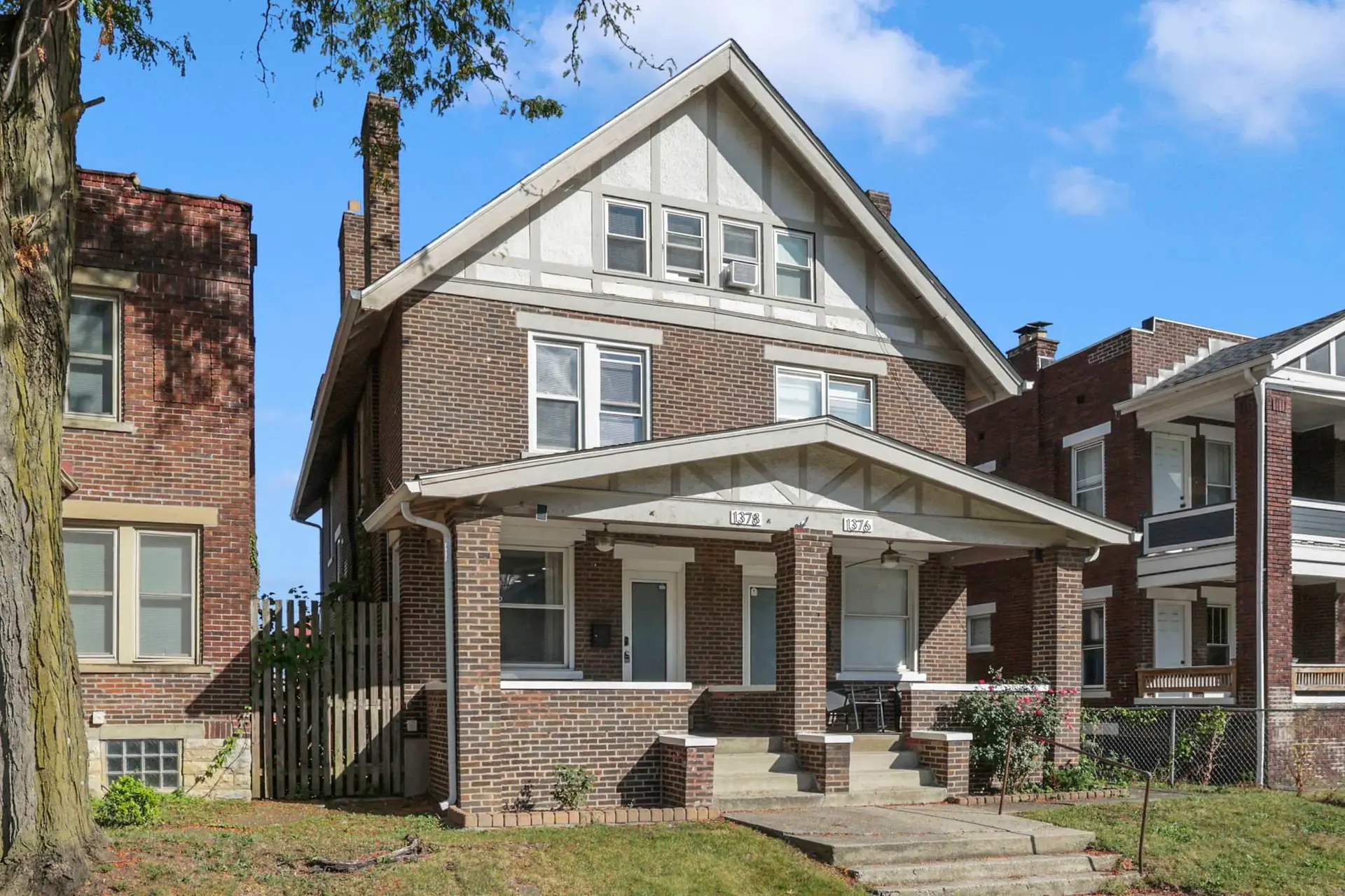 Brick duplex with gabled roof and large porch, on a sunny day.