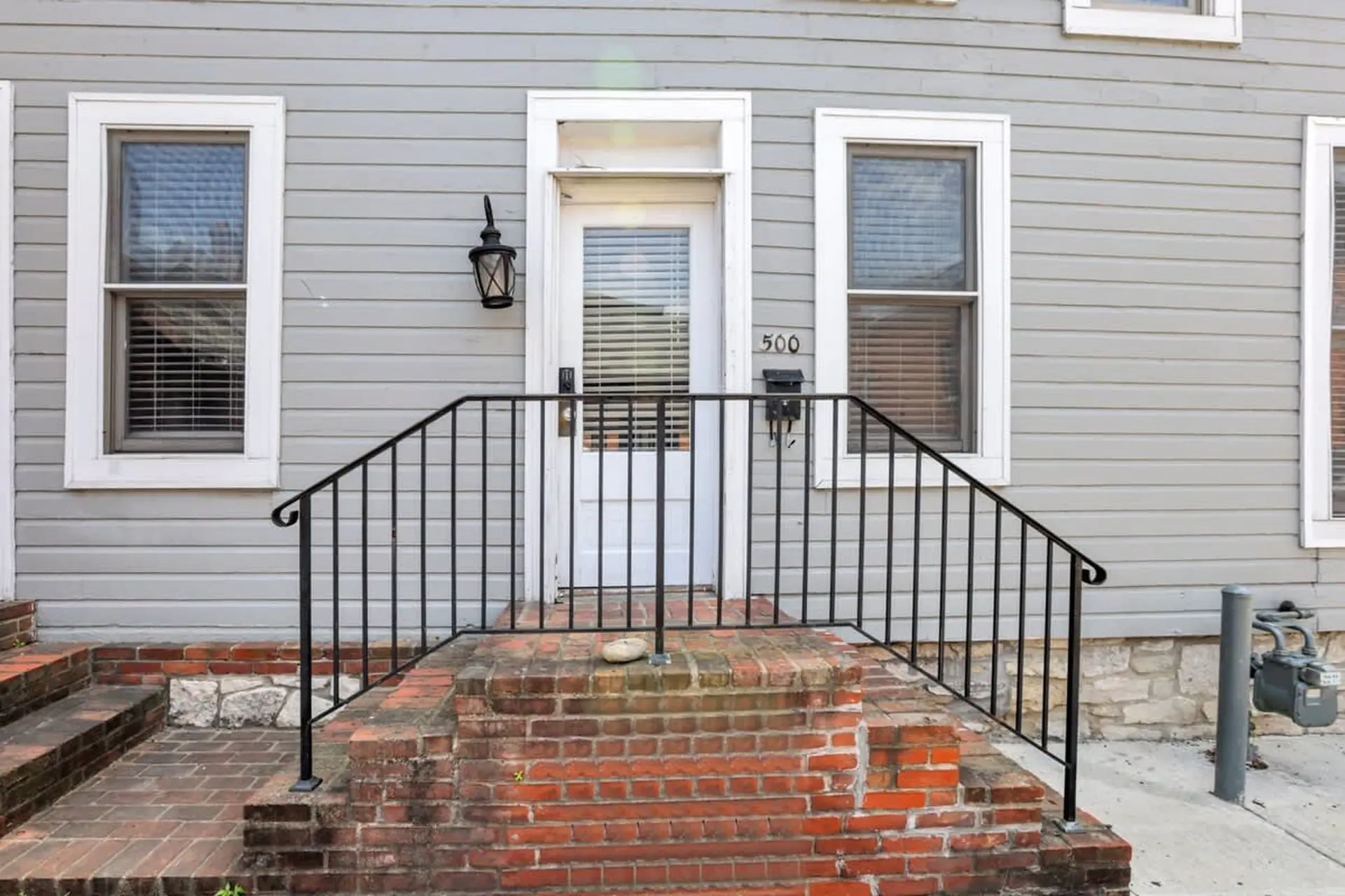 Front view of a house with a white door, two windows, and brick steps.