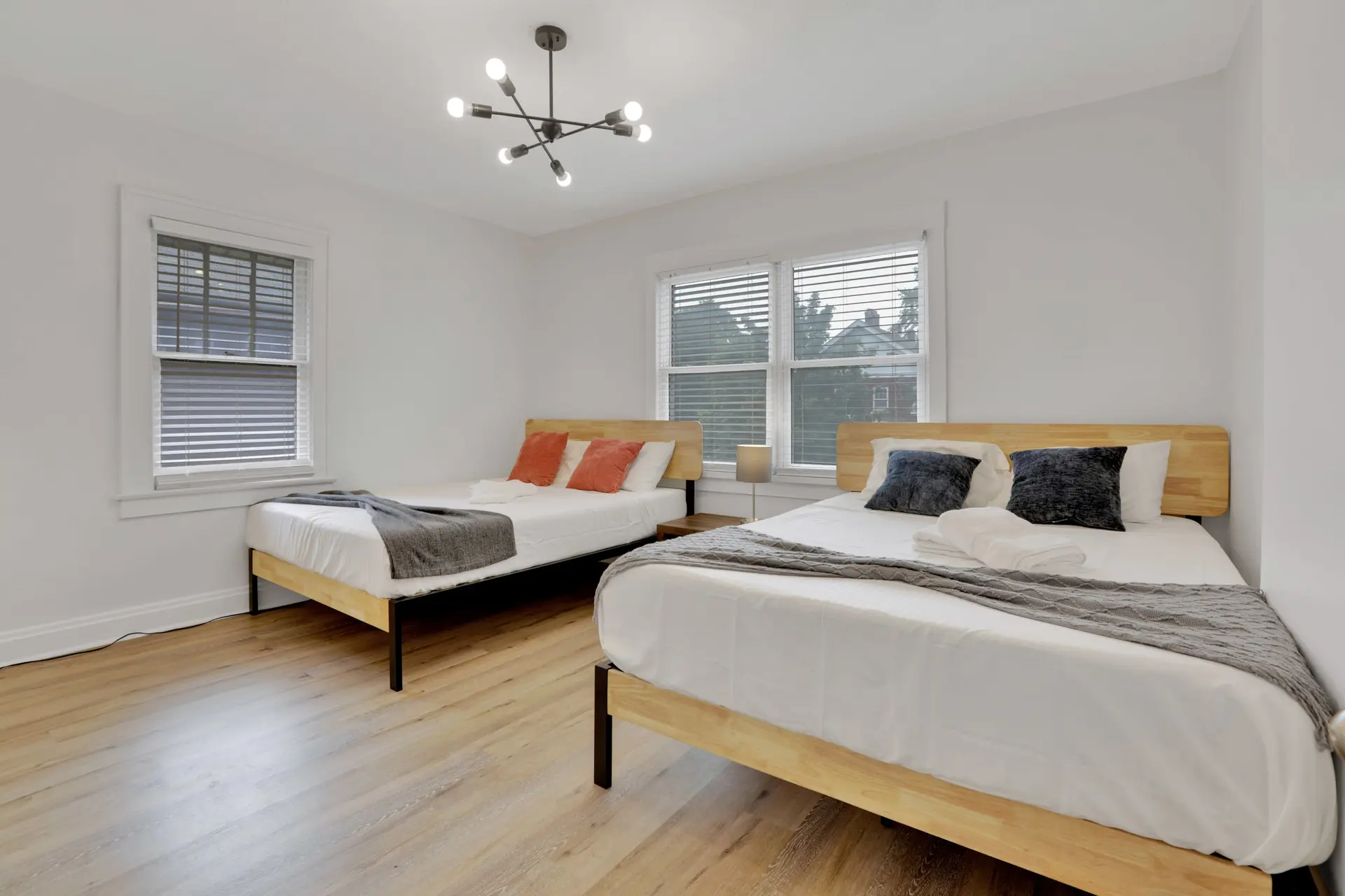 A modern bedroom with two beds, wood flooring, and a Sputnik chandelier.