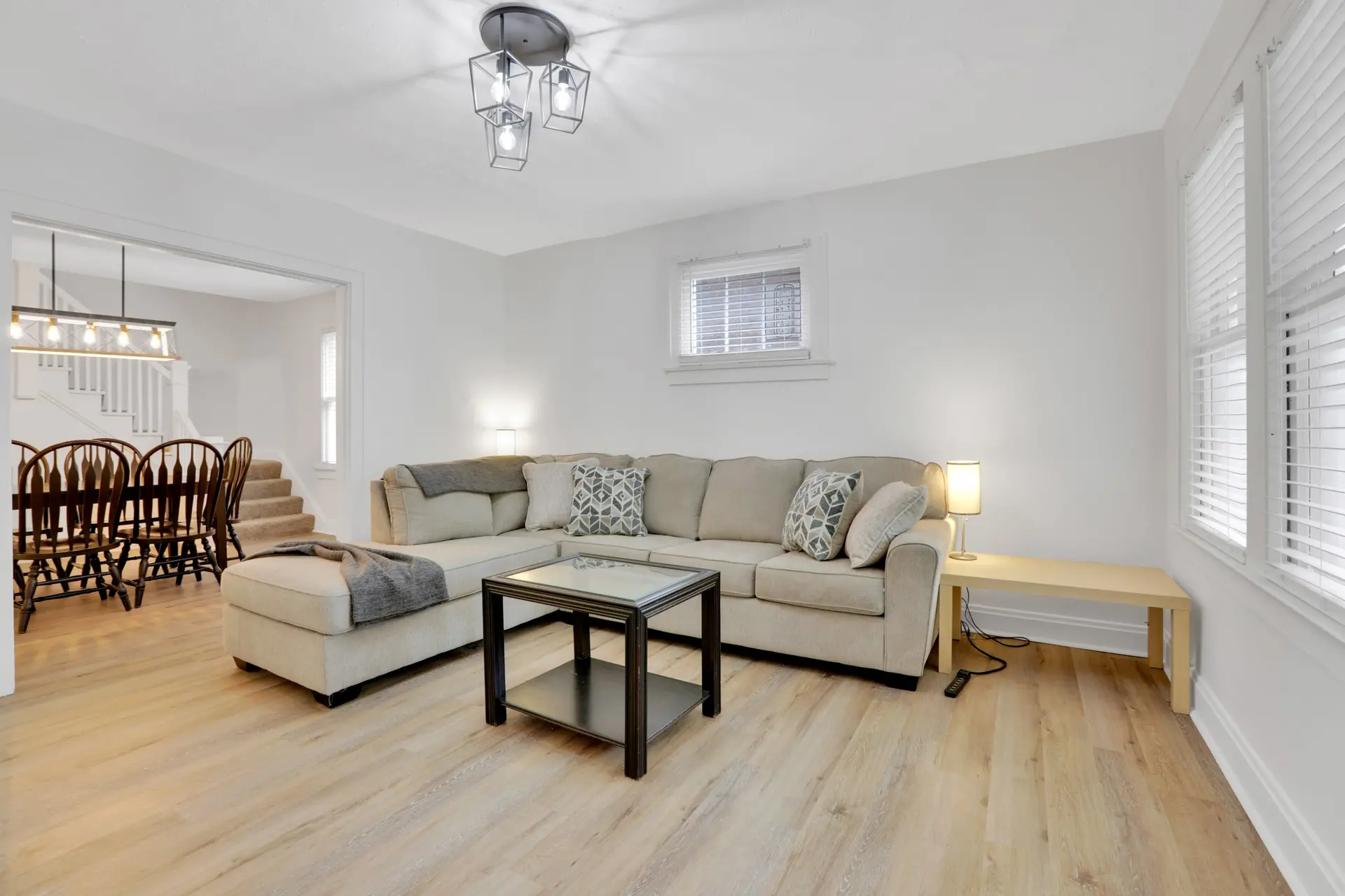 Light-colored sectional couch in a living room with a glass coffee table and wood floors.