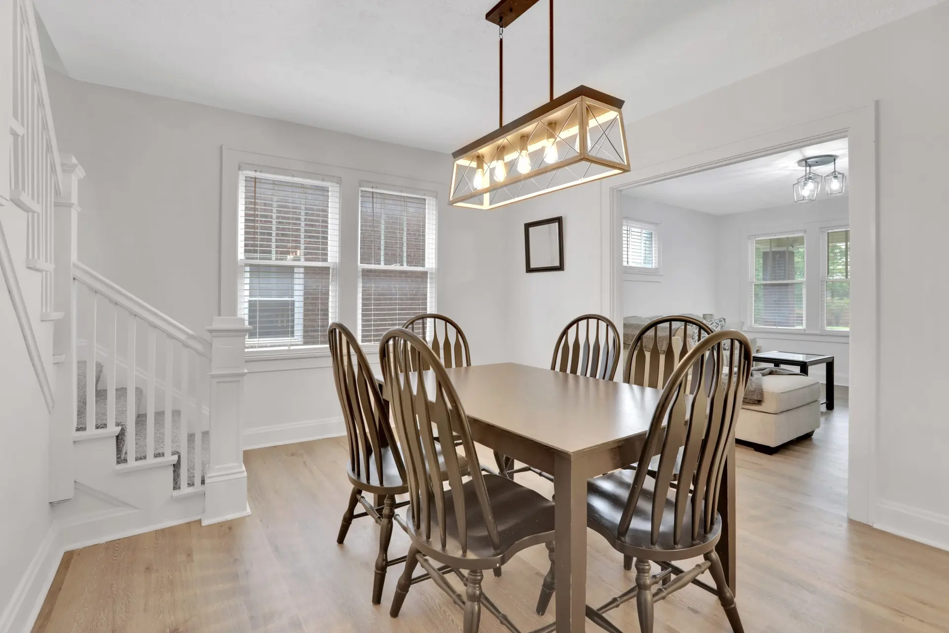 A bright dining room with a wooden table and chairs and a modern chandelier.
