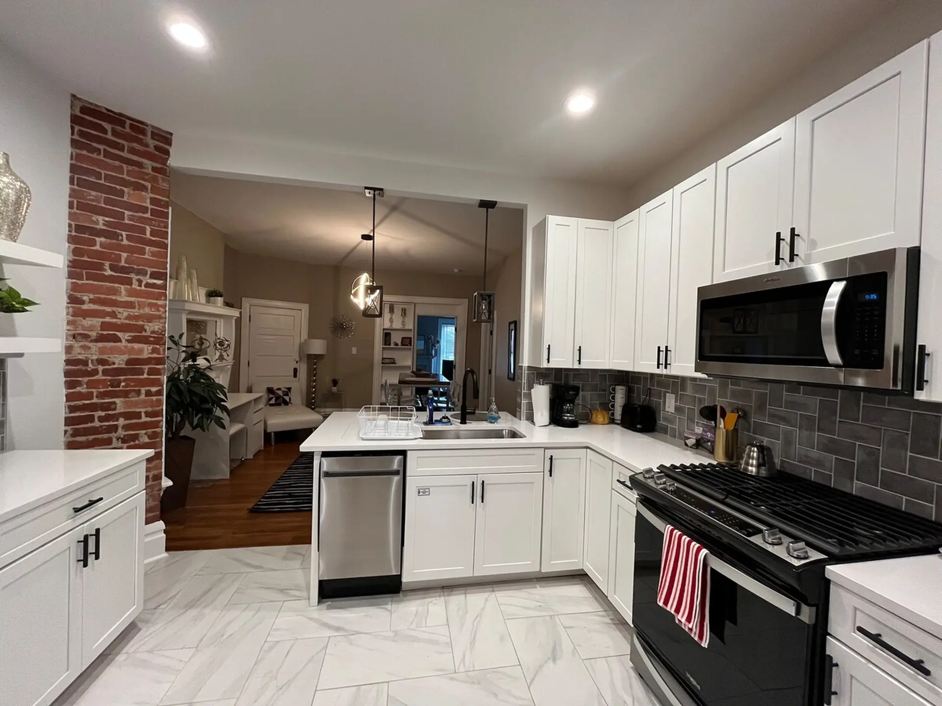 A modern white kitchen with stainless steel appliances and exposed brick.