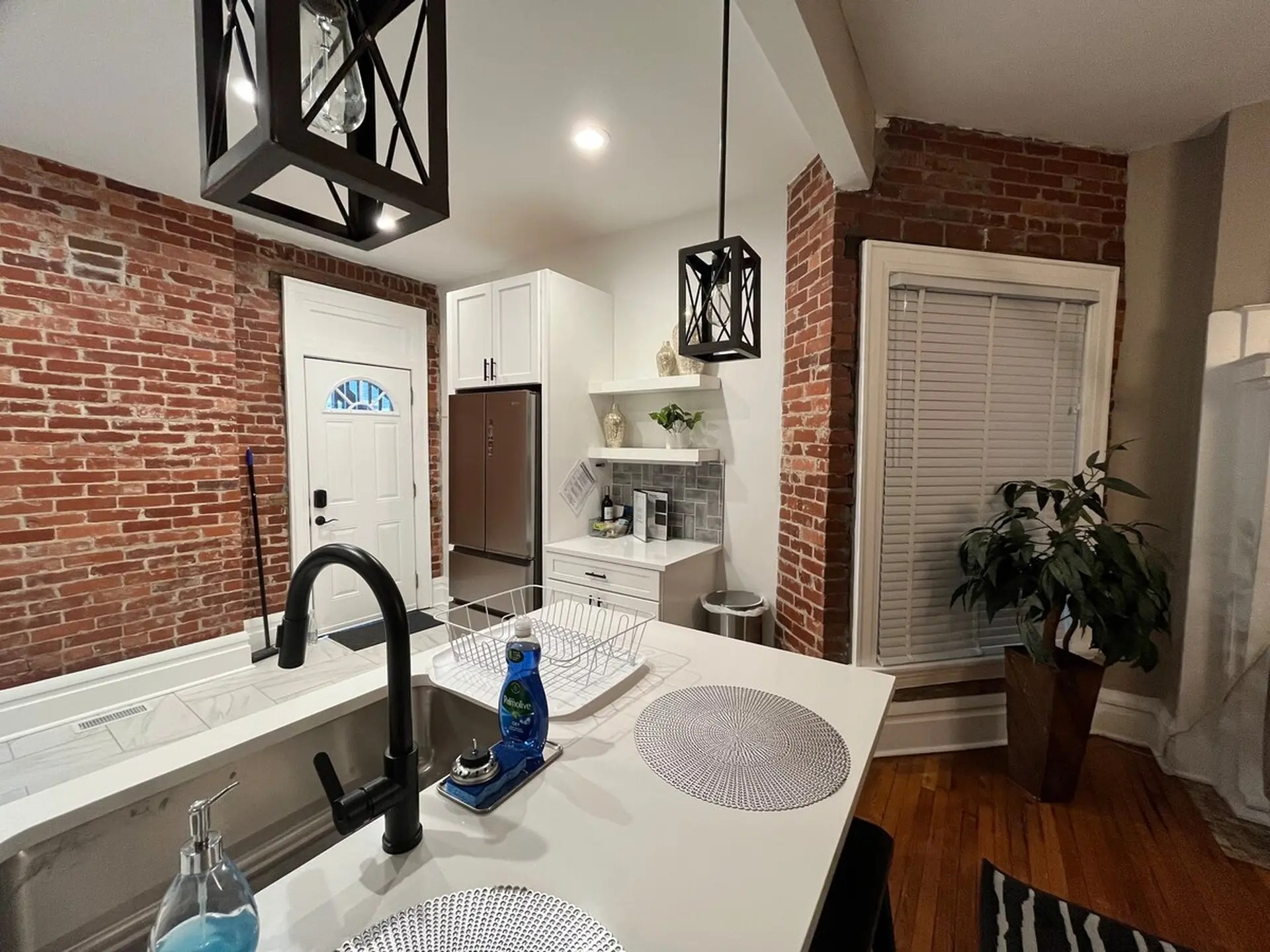 Kitchen with brick walls, a large sink with a black faucet, and white cabinets.