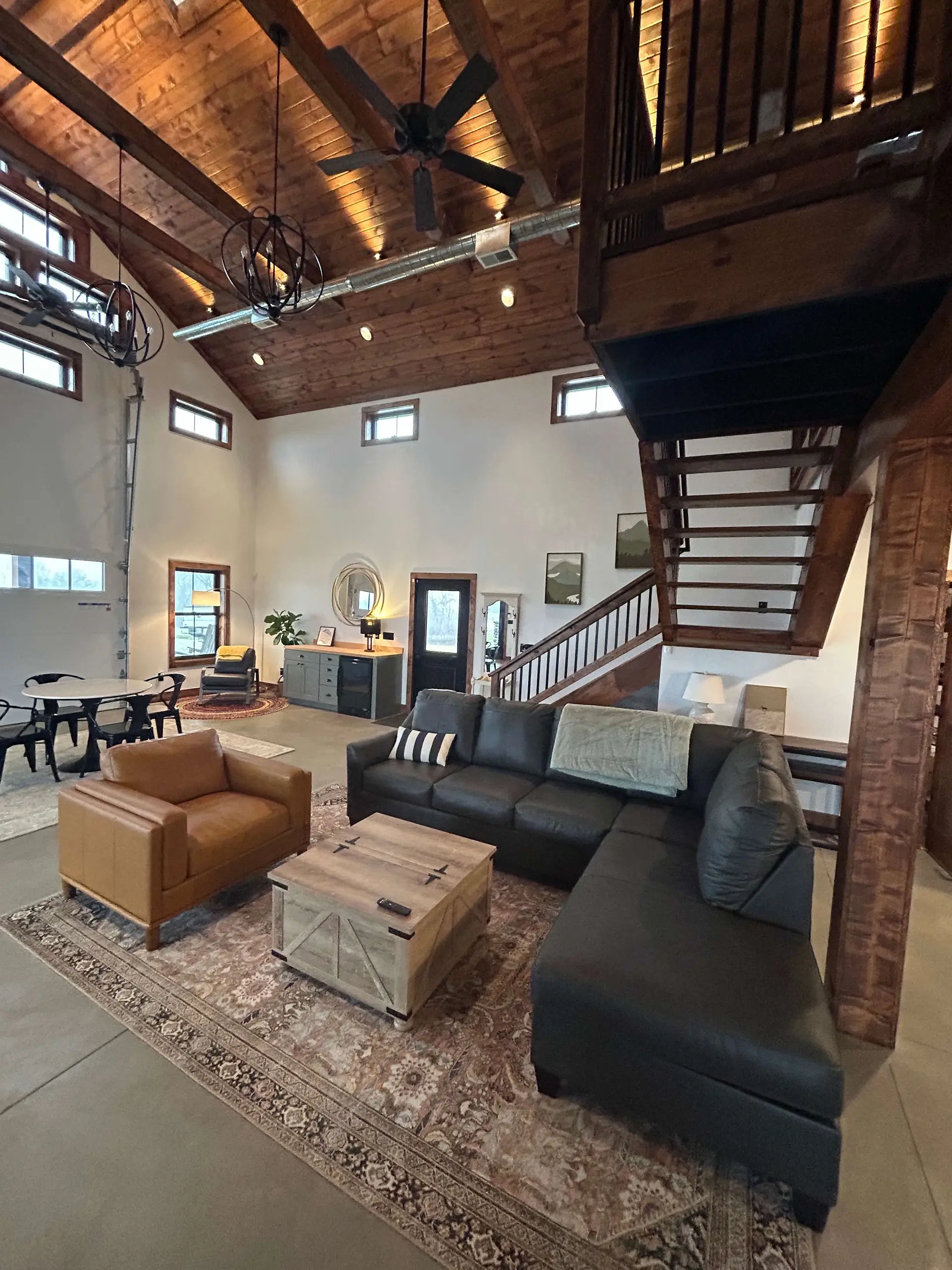 A spacious room with a high, wood-beamed ceiling, a sectional sofa, and a staircase.