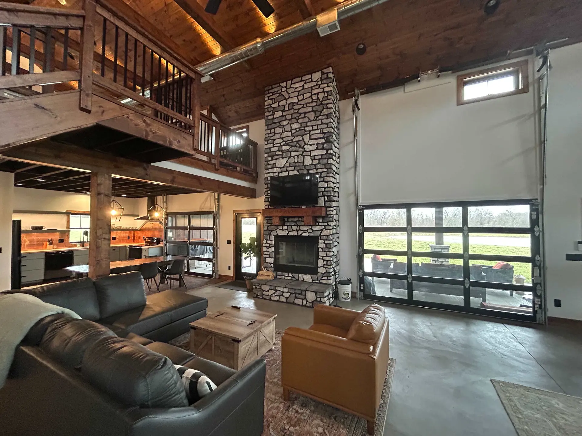 Living room with stone fireplace, leather sofas, wooden beams, and large glass doors.