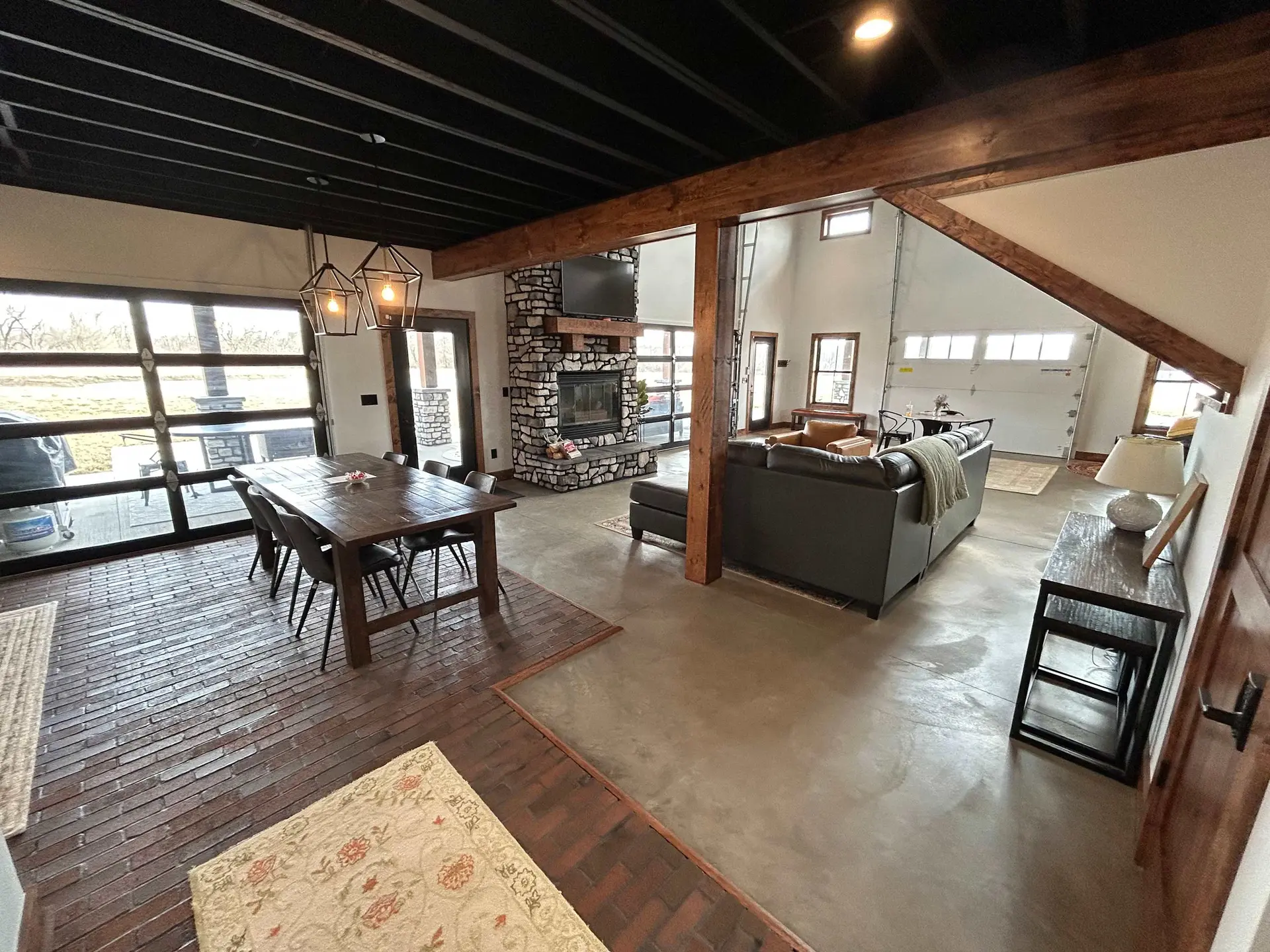 The image shows a modern living and dining area with a stone fireplace and large windows.