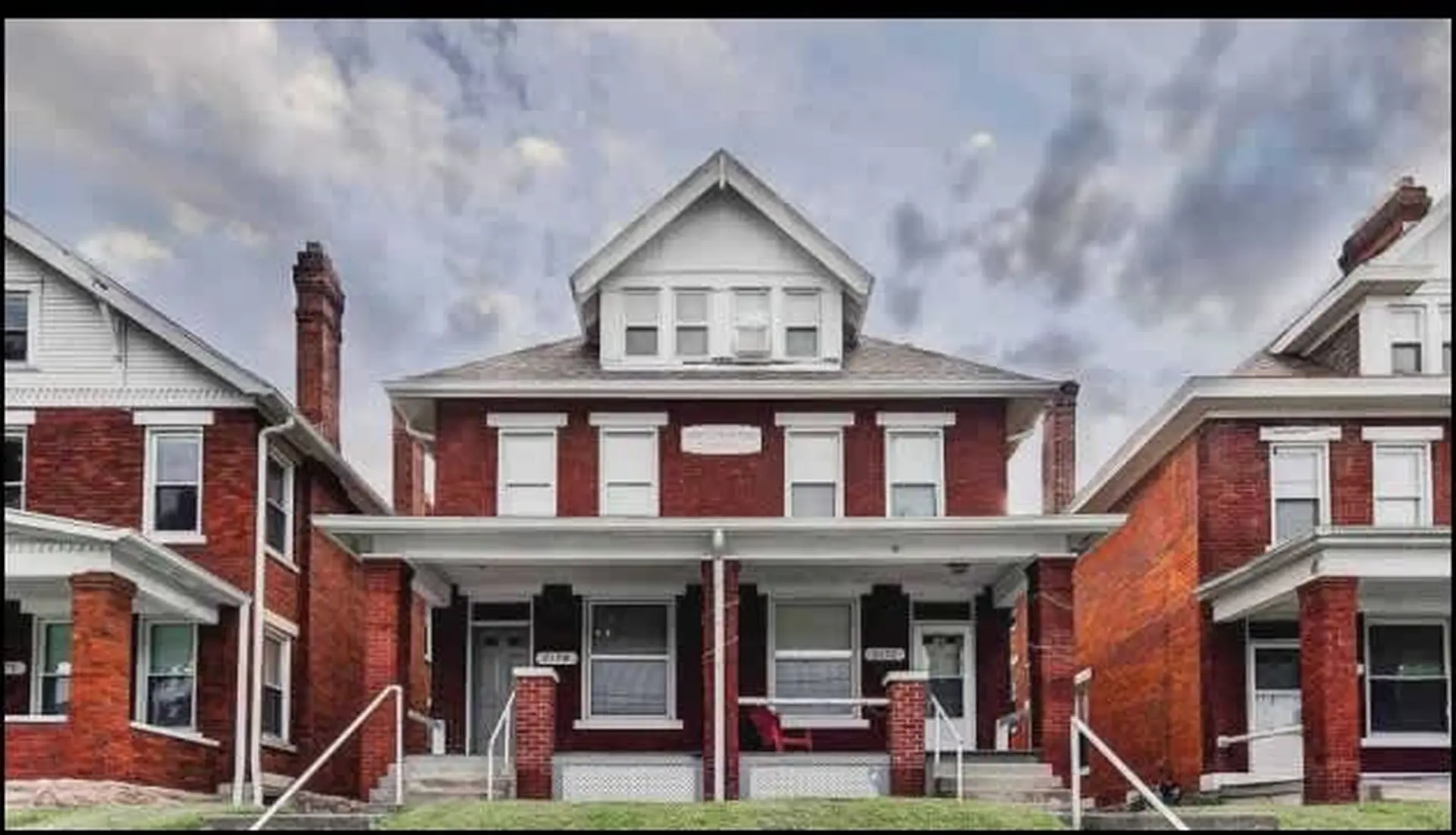 Three brick houses under a cloudy sky.