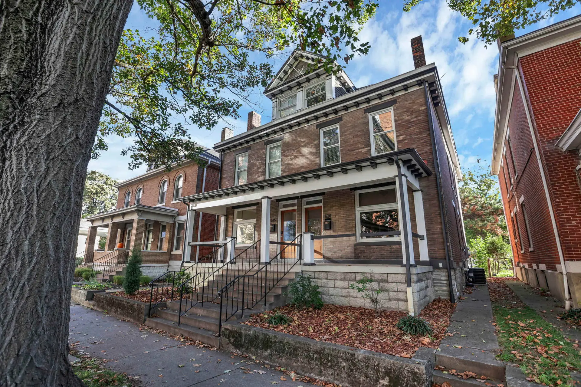Brick houses with porches and trees on a sunny day.