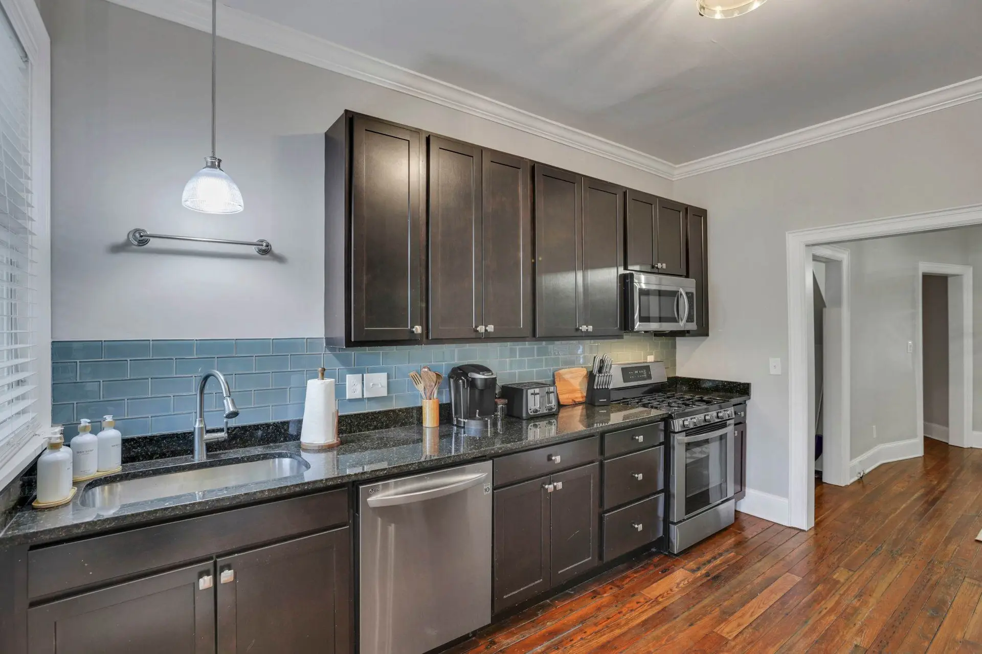 A modern kitchen with dark wood cabinets, stainless steel appliances, and a blue tile backsplash.