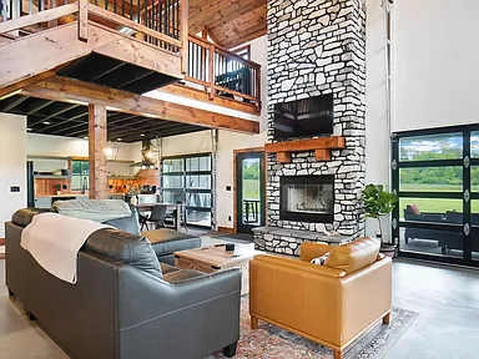 A living room with a stone fireplace, two couches, a TV, and large glass doors.