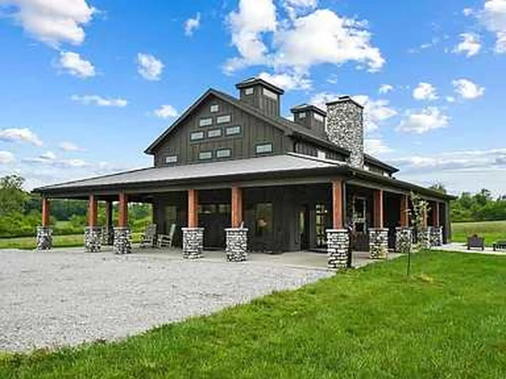 The image shows a modern barn-style house with dark siding and a large, covered porch.