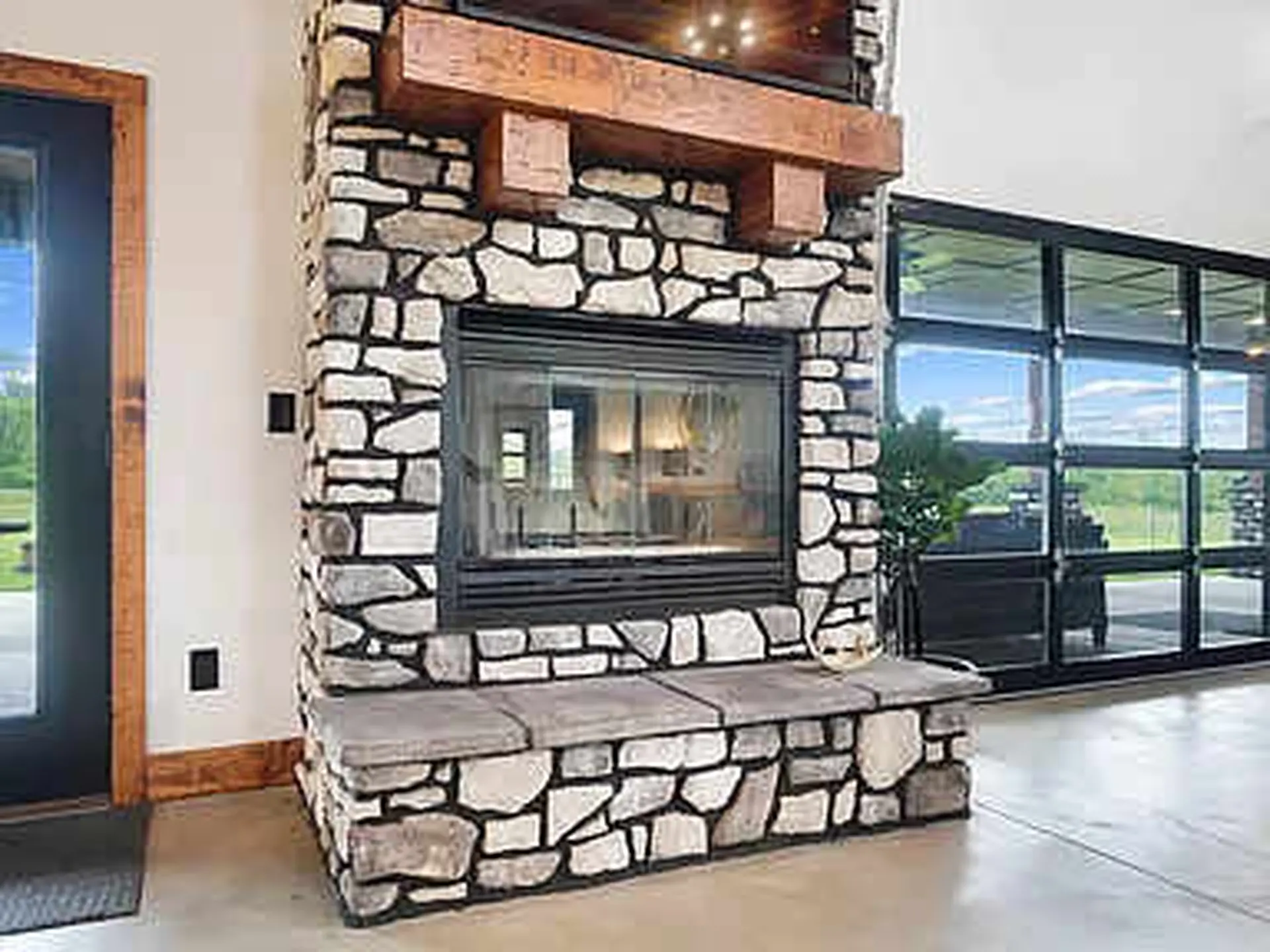 This image shows a stone fireplace with a wooden mantel and a bench.