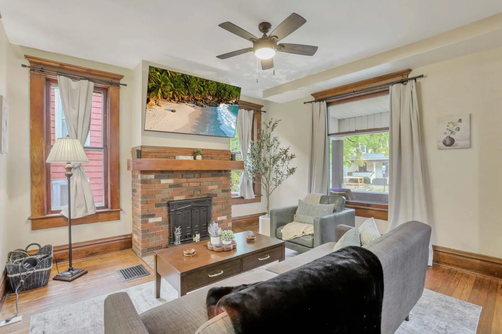 A modern living room with a brick fireplace, a TV, and a ceiling fan.