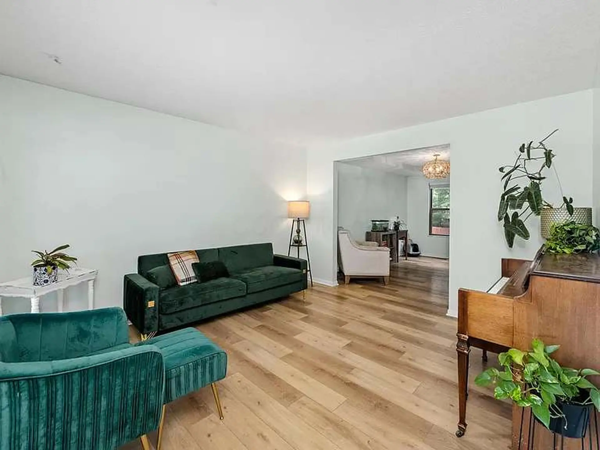 This is a living room with a sofa, armchair, piano, and plants.