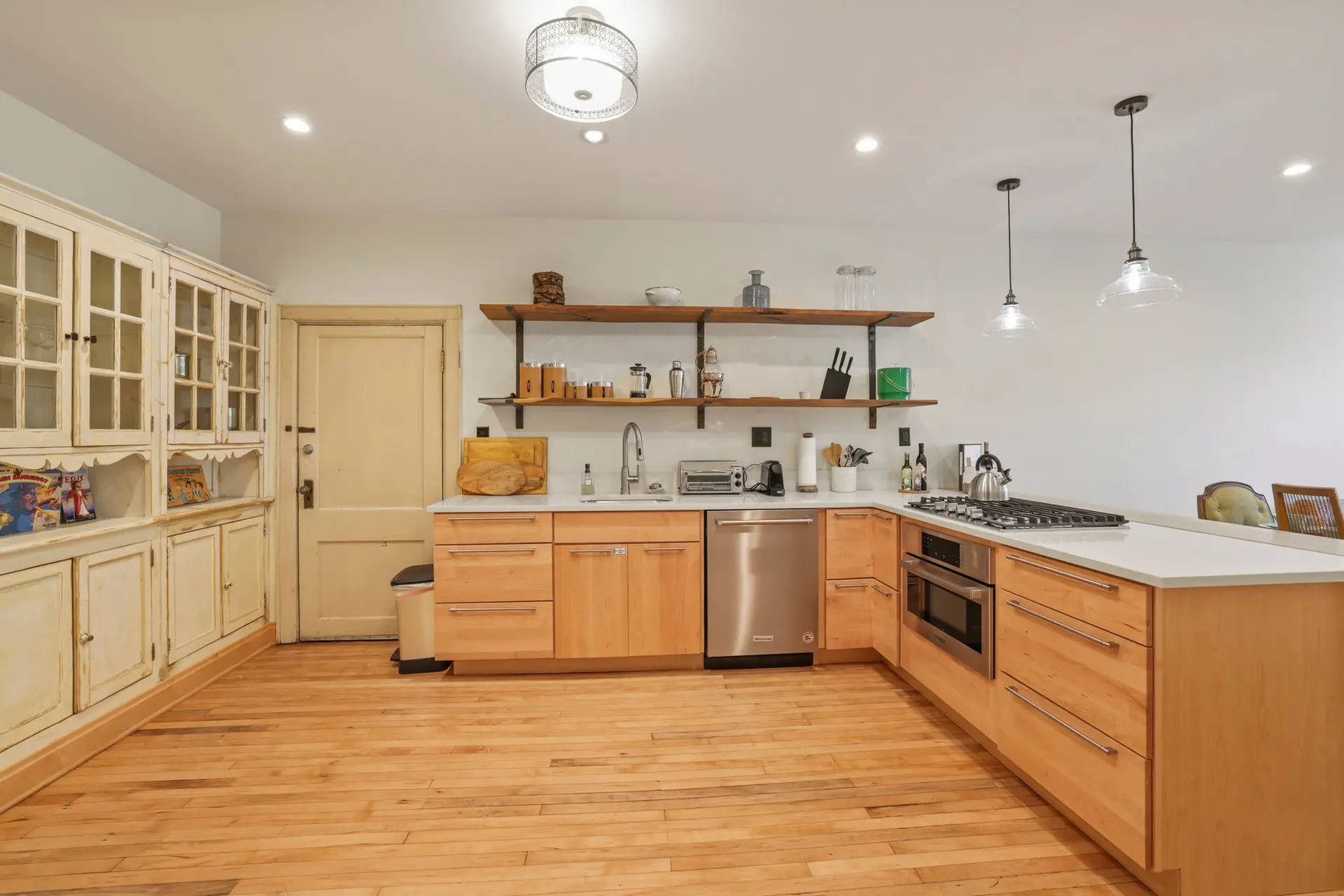 A kitchen with light wood cabinets, white countertops, and a gas stovetop.